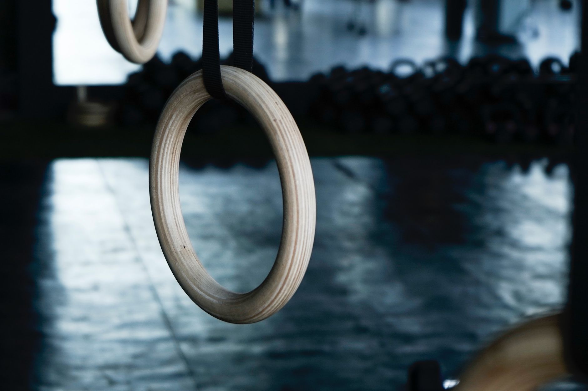 Wooden gym rings hanging in a dimly lit gym, symbolizing fitness and training.
