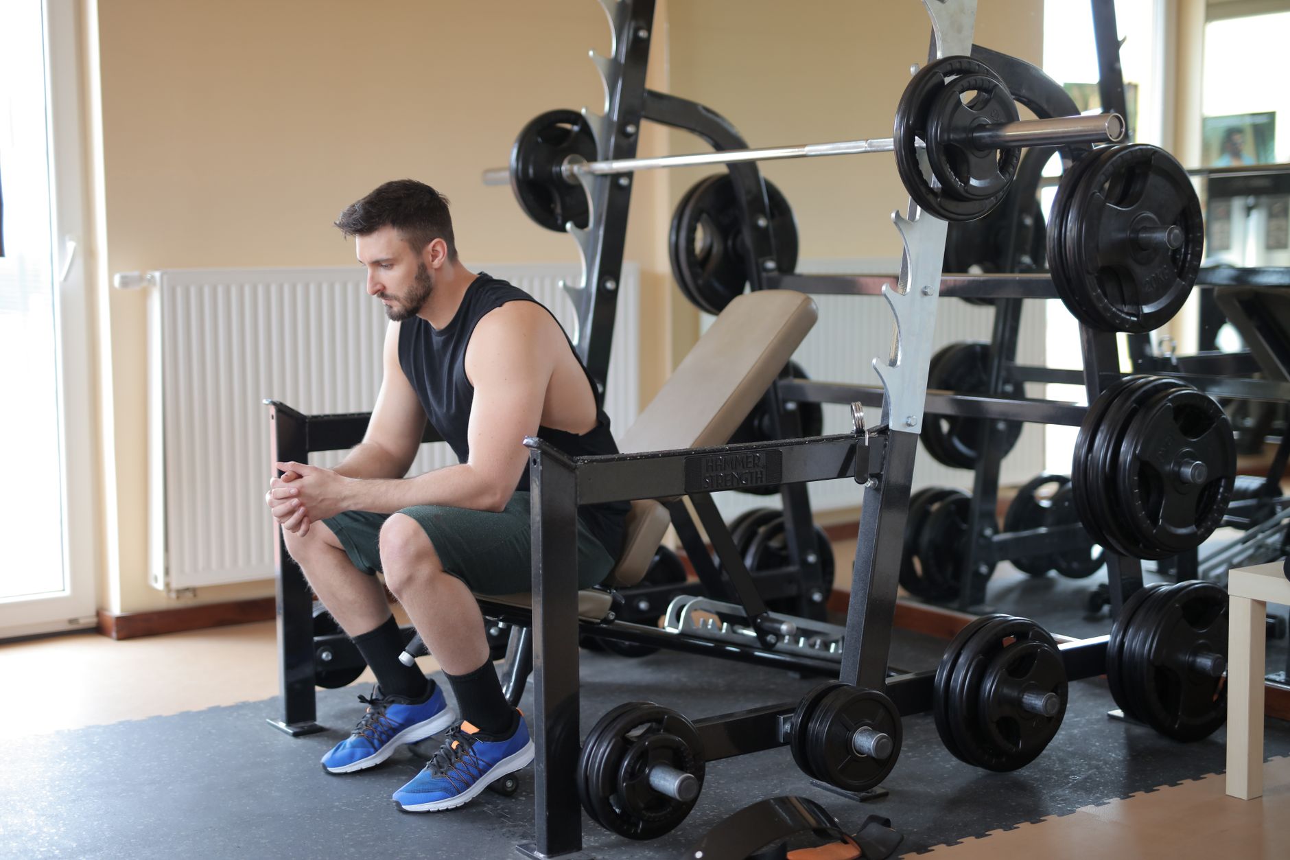 A man takes a break at the gym sitting beside a fully loaded barbell, showcasing strength.