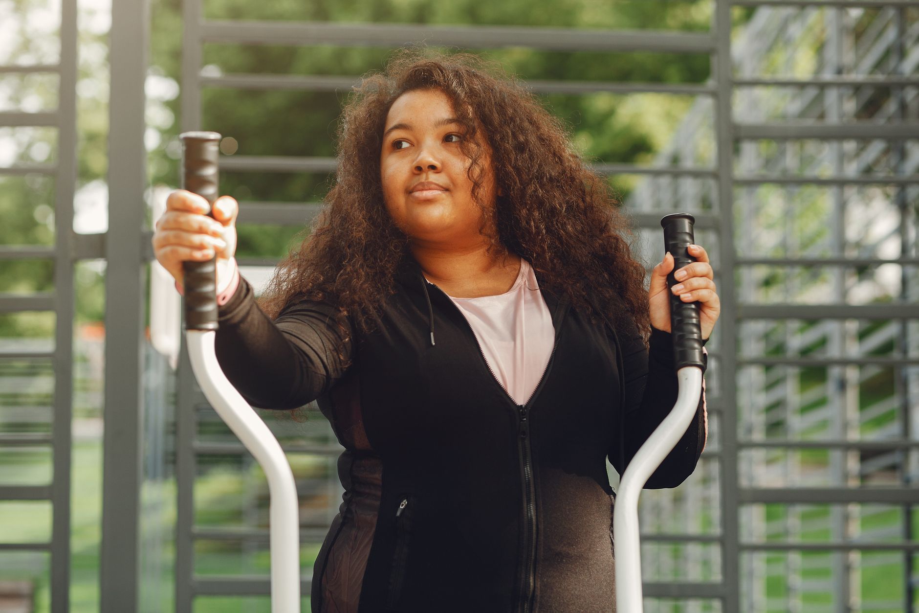 Young woman using outdoor elliptical trainer in a park.