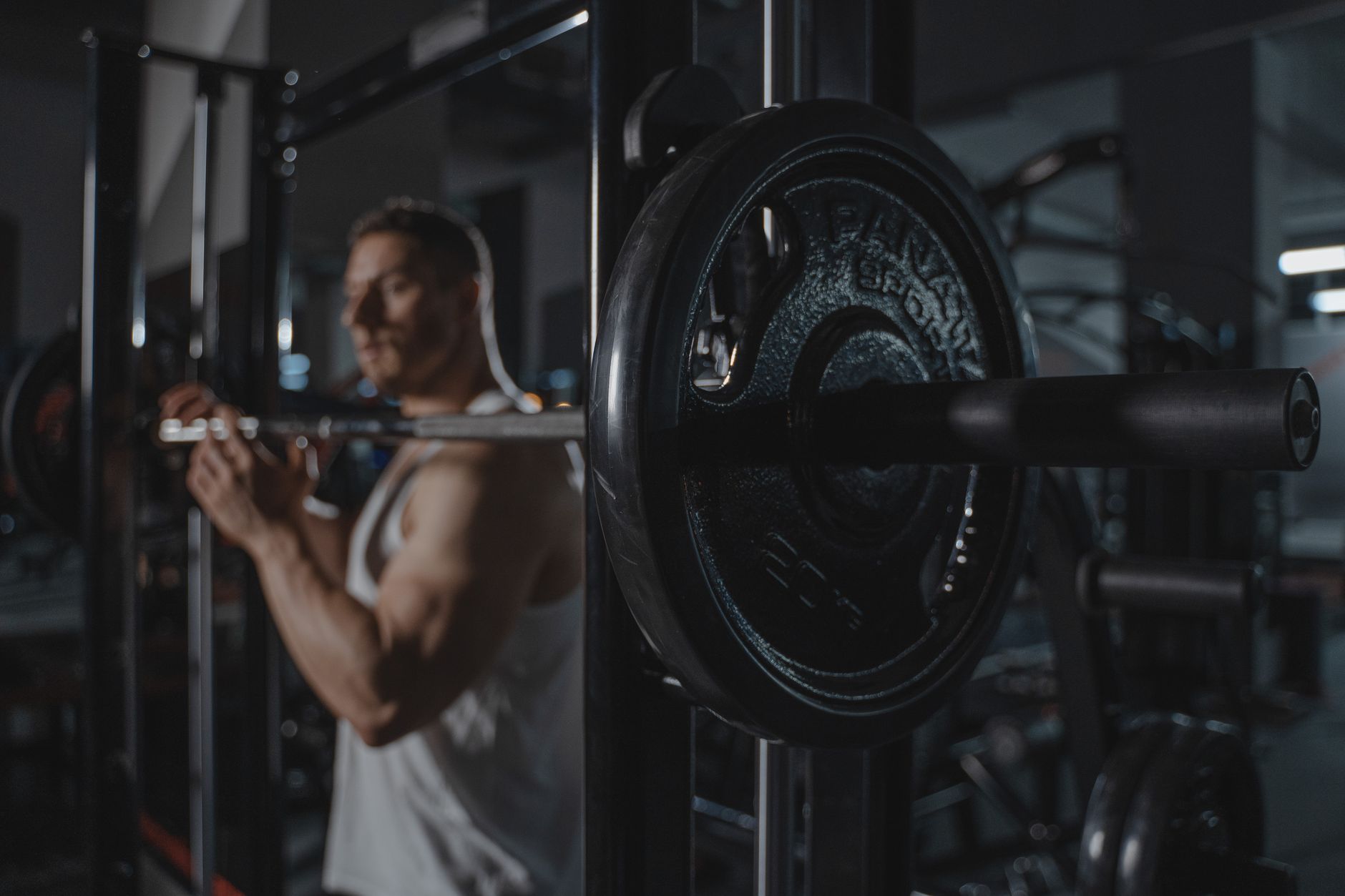 Muscular man lifting a barbell in a dimly lit gym setting.
