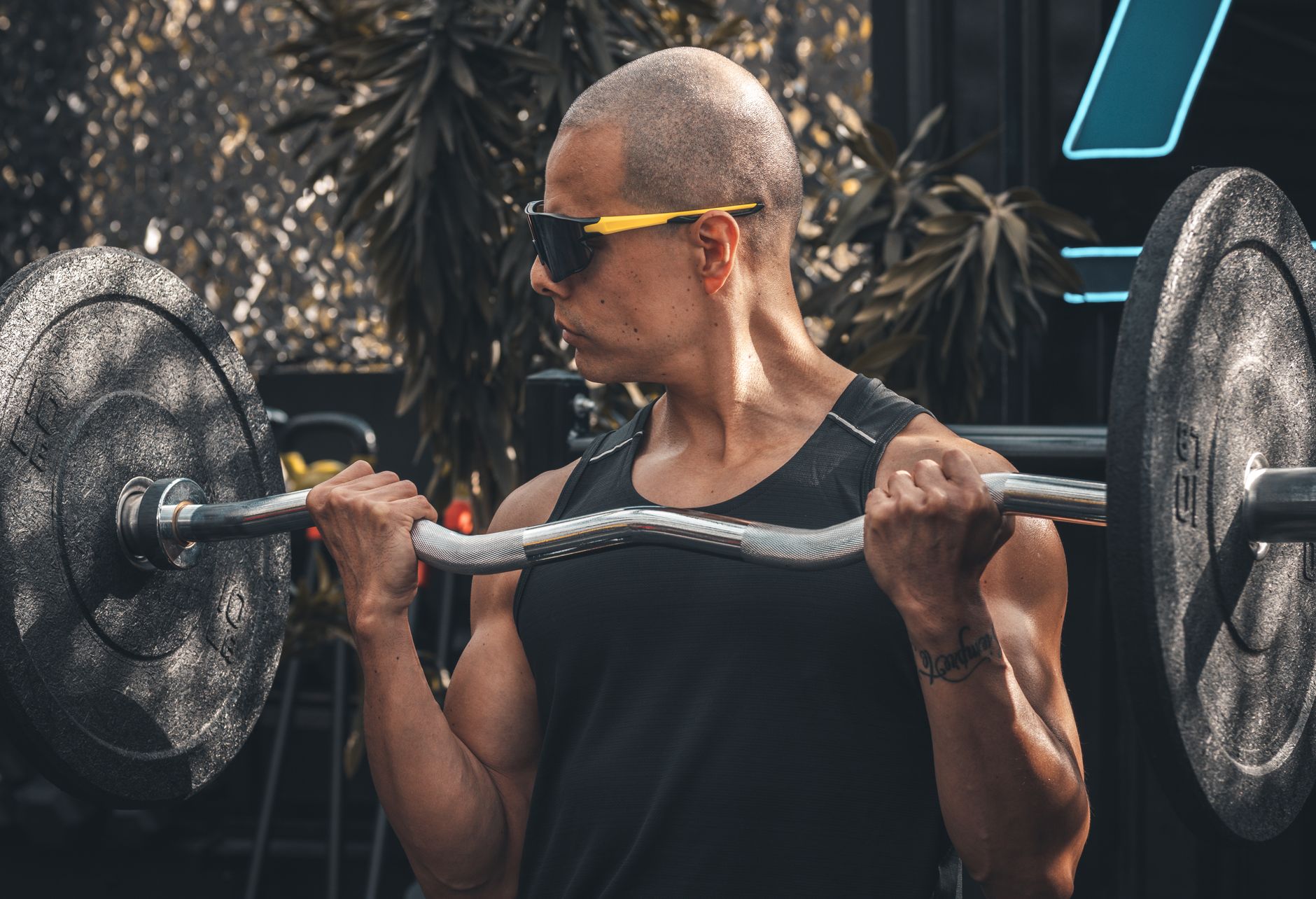 A muscular man lifts a barbell in an outdoor gym setting, showcasing strength and fitness.