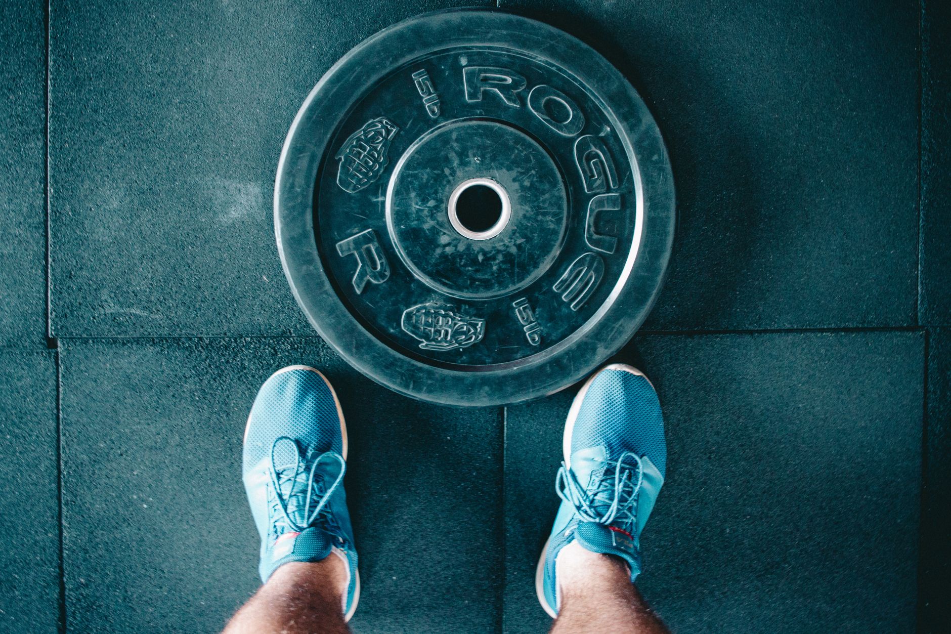Blue sneakers next to a weight plate on a gym floor, top view.