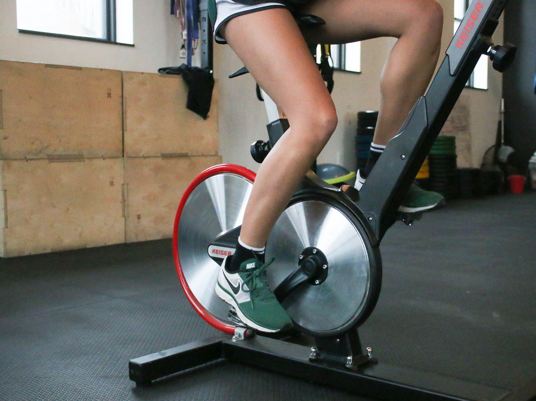 From below of anonymous crop person in shorts and sneakers exercising on stationary bike while training in gym