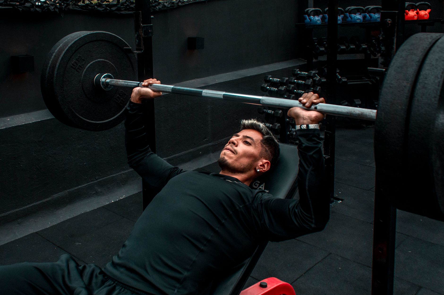 Man performing bench press with heavy barbell in a gym setting, focusing on strength training.