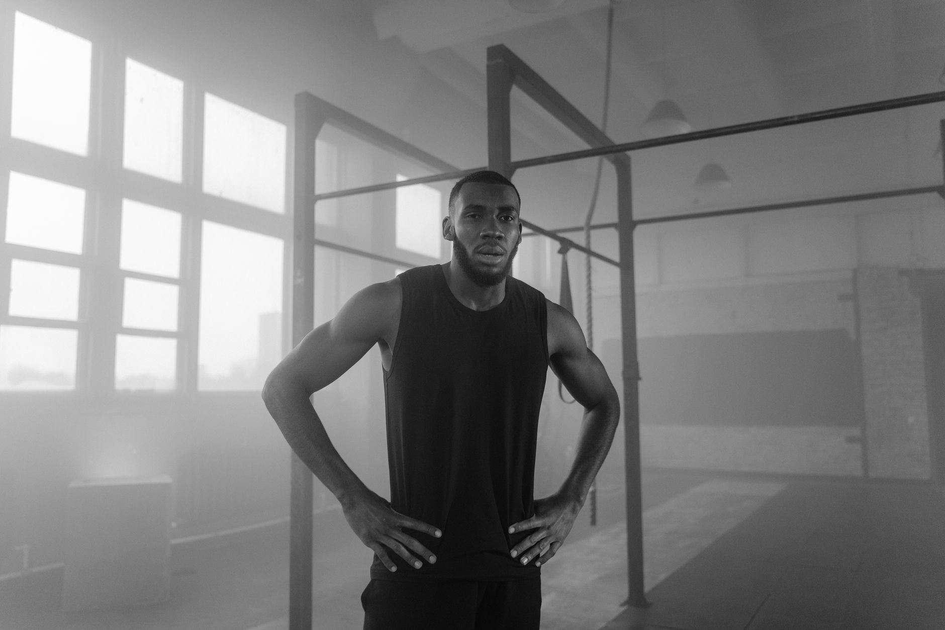 Black and white photo of a focused athlete standing in a gym with misty ambiance.