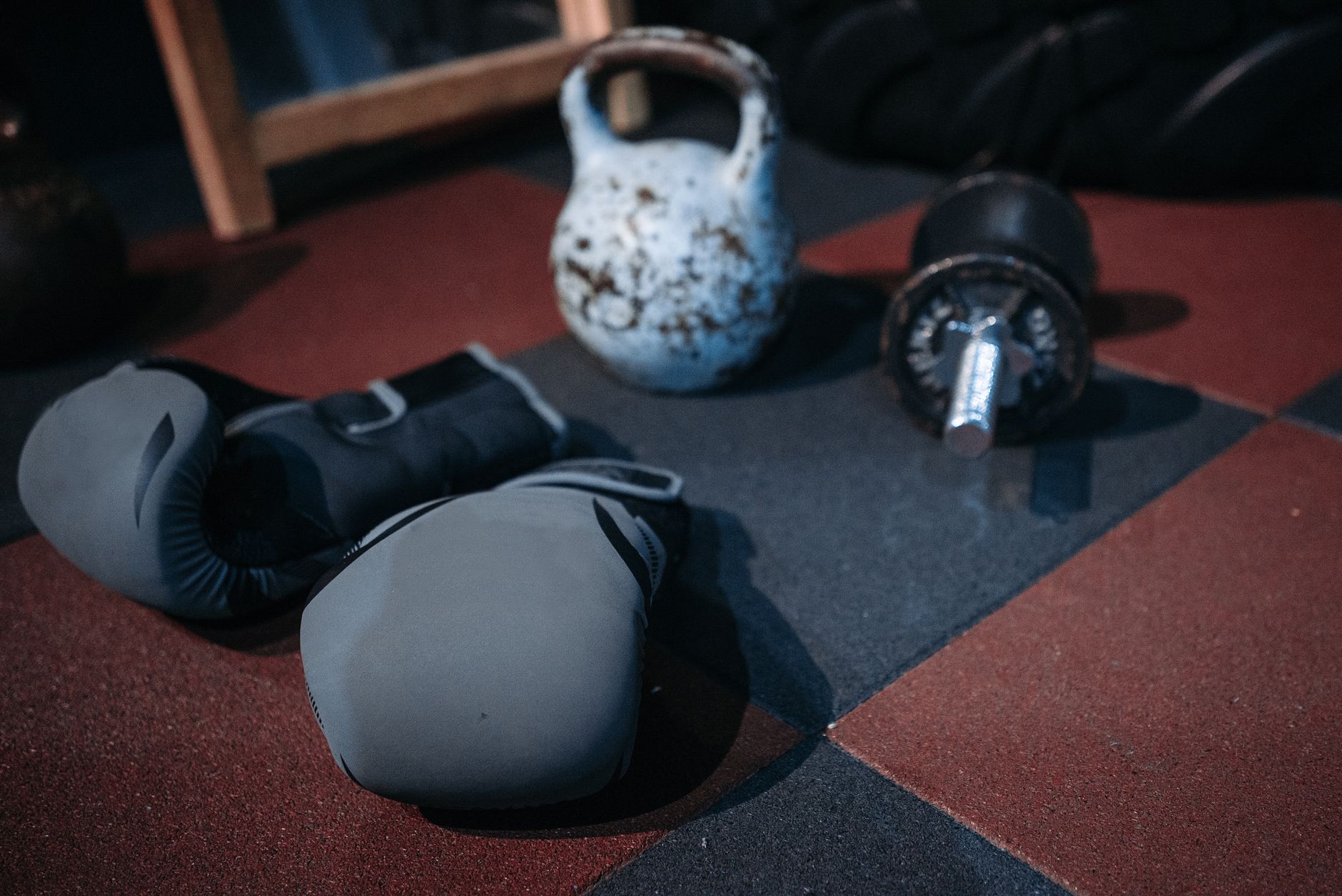 Close-up of gym equipment including a kettlebell, dumbbell, and boxing gloves on a gym floor.