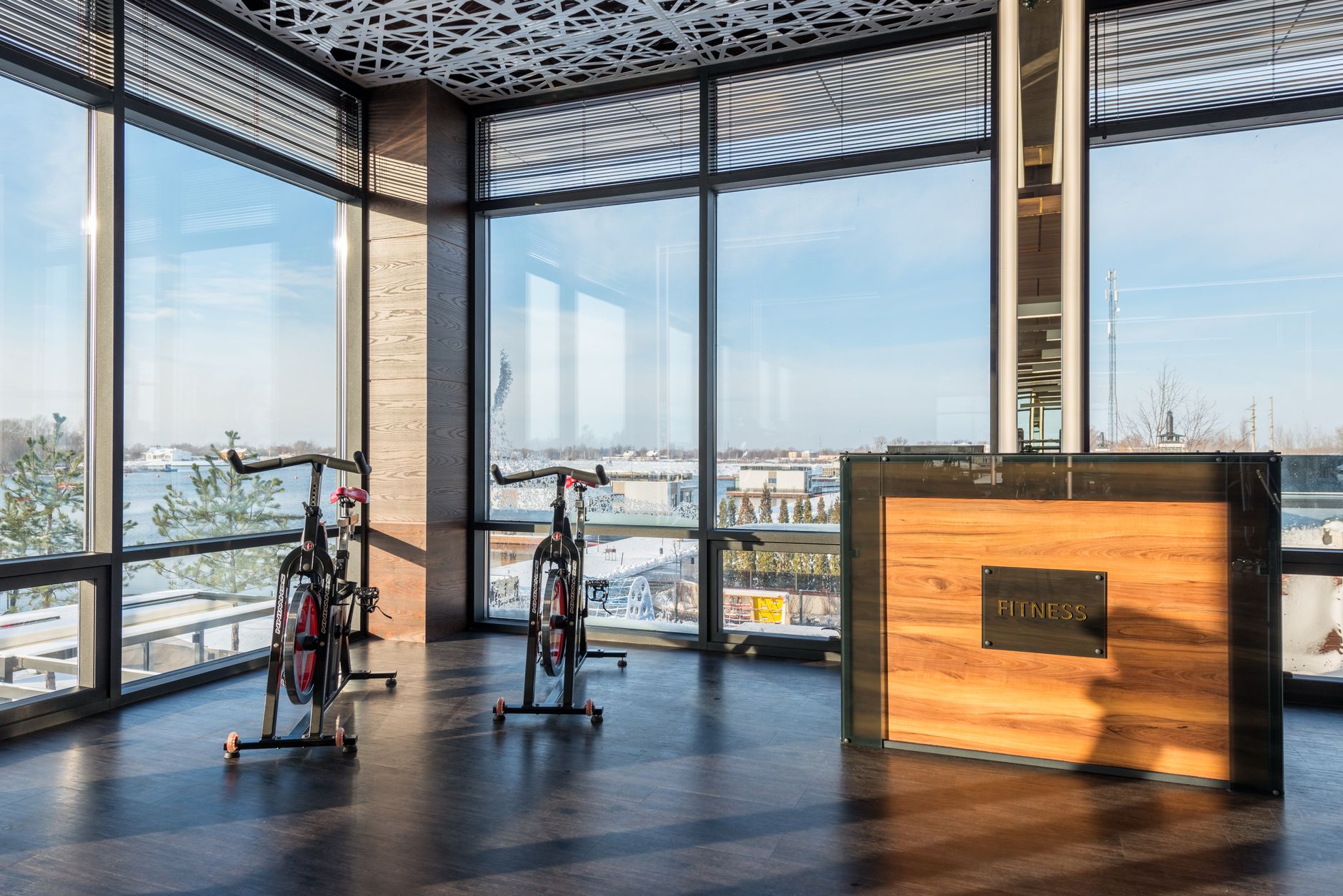 Modern exercise bikes and wooden reception desk near panoramic windows of spacious gym in sunlight