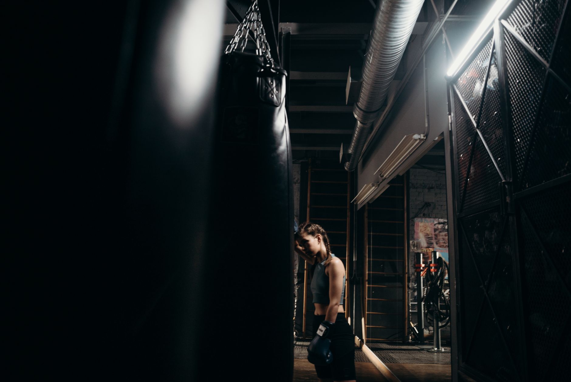 A strong female boxer intensely trains with a punching bag in an industrial-style gym.