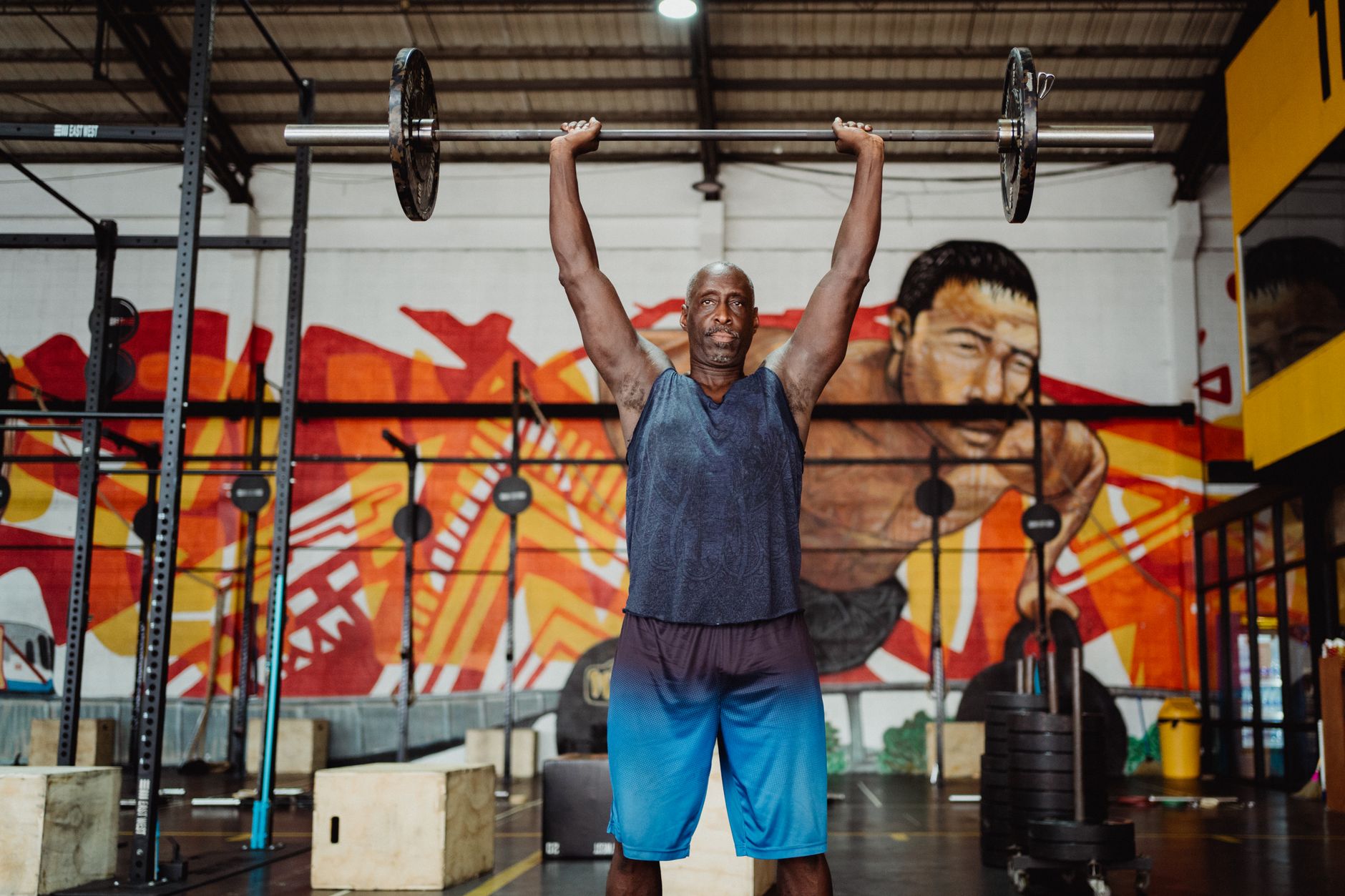 A strong man lifting a barbell in a vibrant gym with murals.