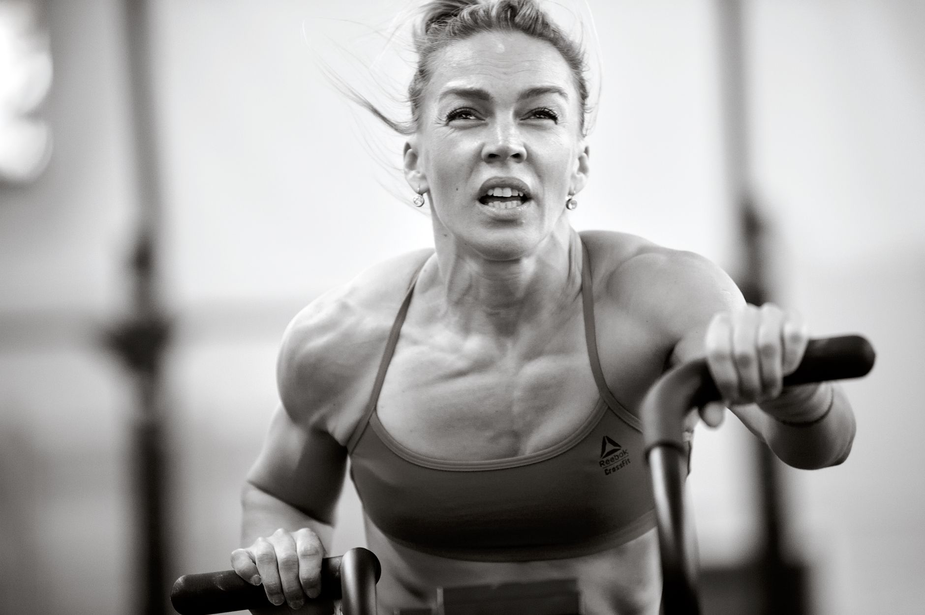A focused woman in a sports bra intensely working out on exercise equipment, showcasing fitness and determination.