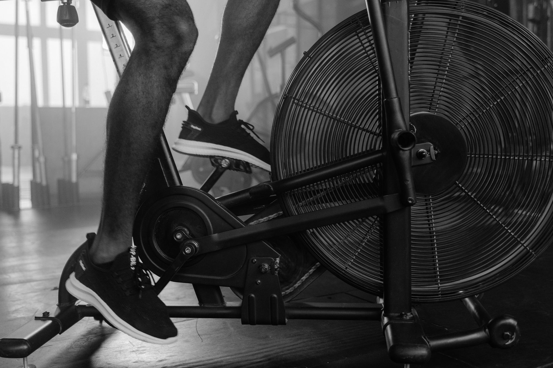 Black and white image of person using exercise bike in a gym setting.