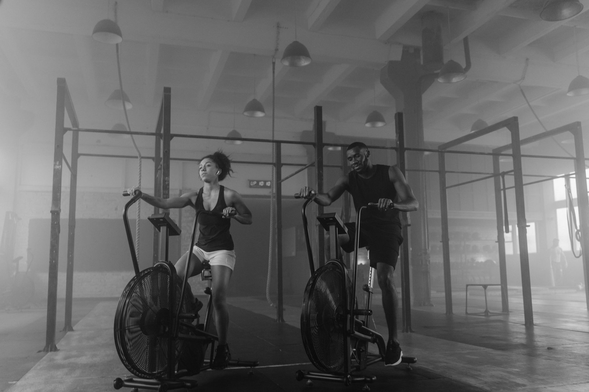 A fit couple exercising on air bikes in a gym setting.