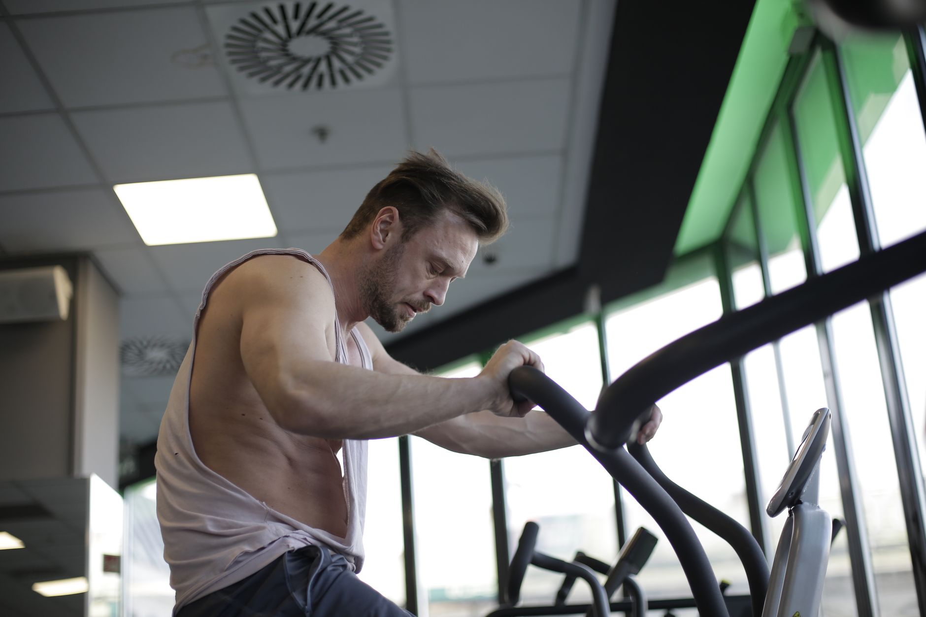 Side view of muscular adult male athlete in sportswear during training on exercise bike in modern spacious fitness center in morning