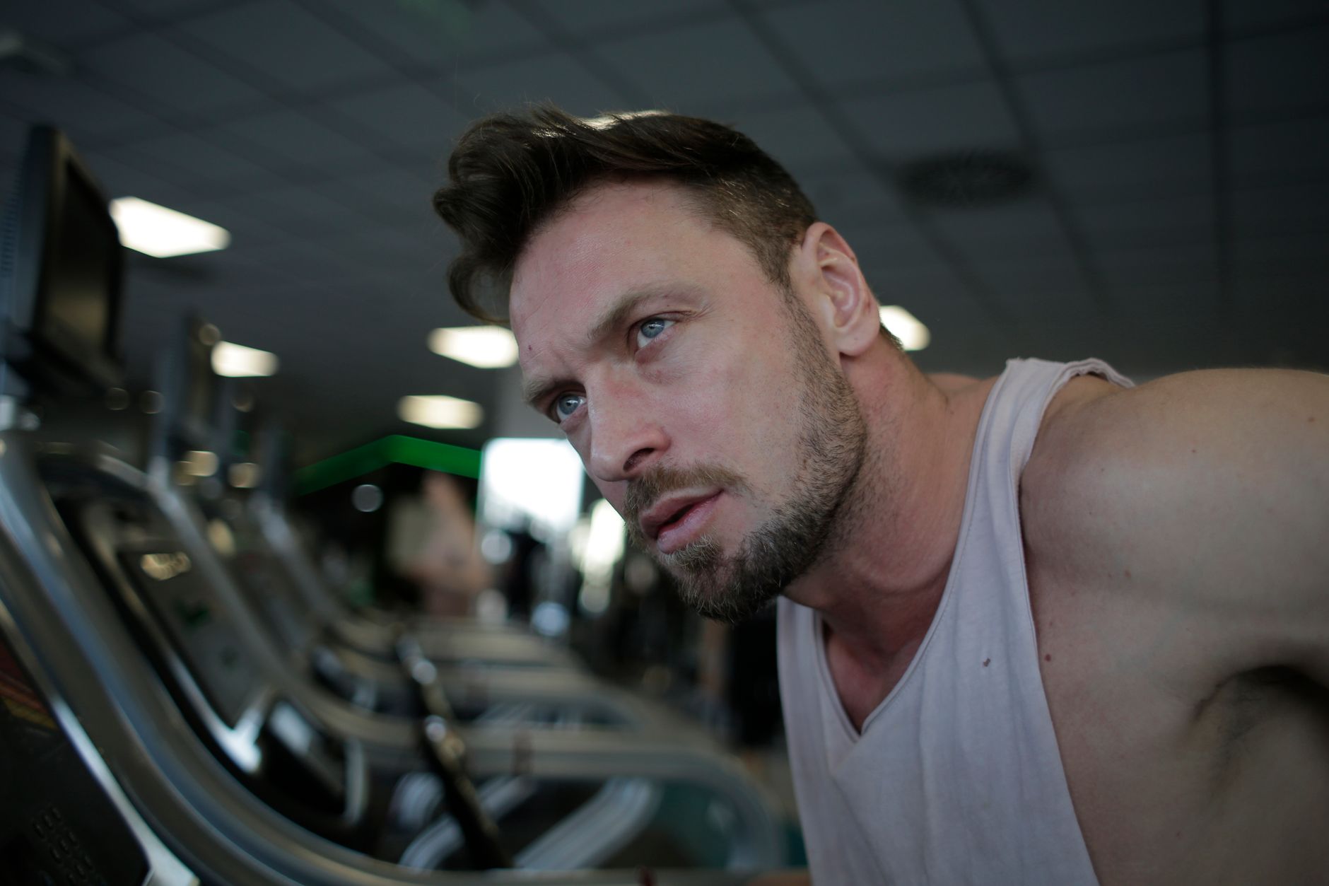 A pensive man with facial hair working out on a treadmill indoors for fitness and health.