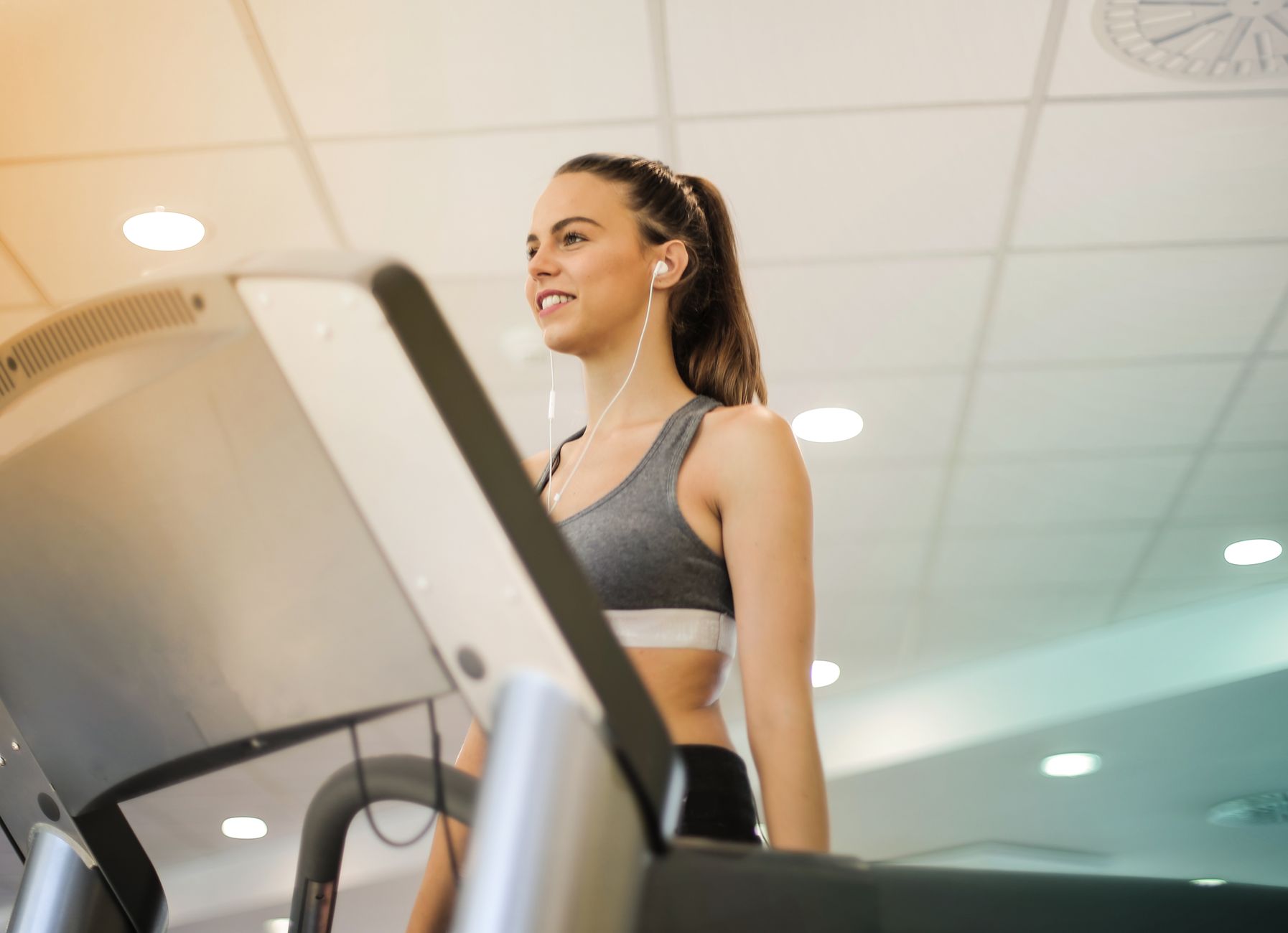 Fit woman running on treadmill in gym wearing sports bra and earphones.