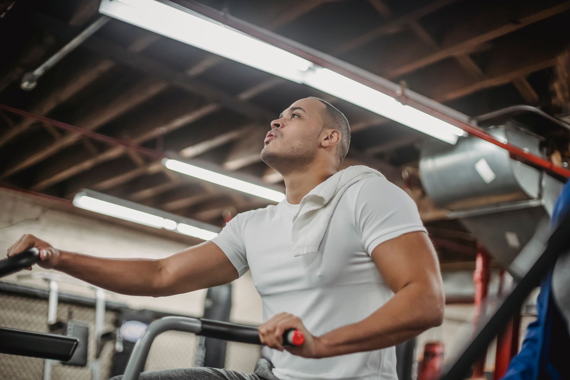 Muscular ethnic sportsman cycling on stationary bike while working out in equipped gym