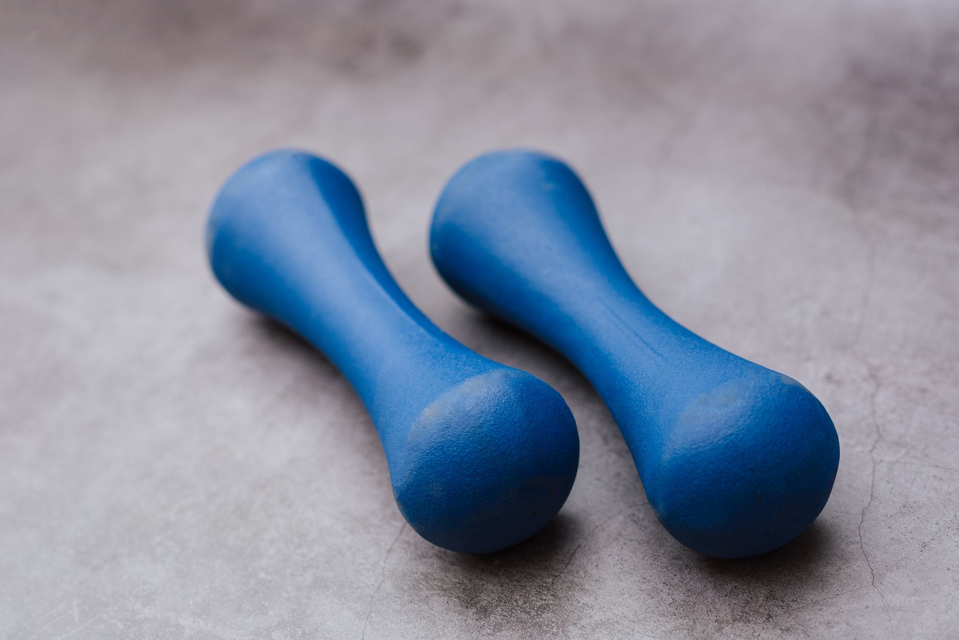 From above of pair of dumbbells with solid texture and bright blue coating on grey floor