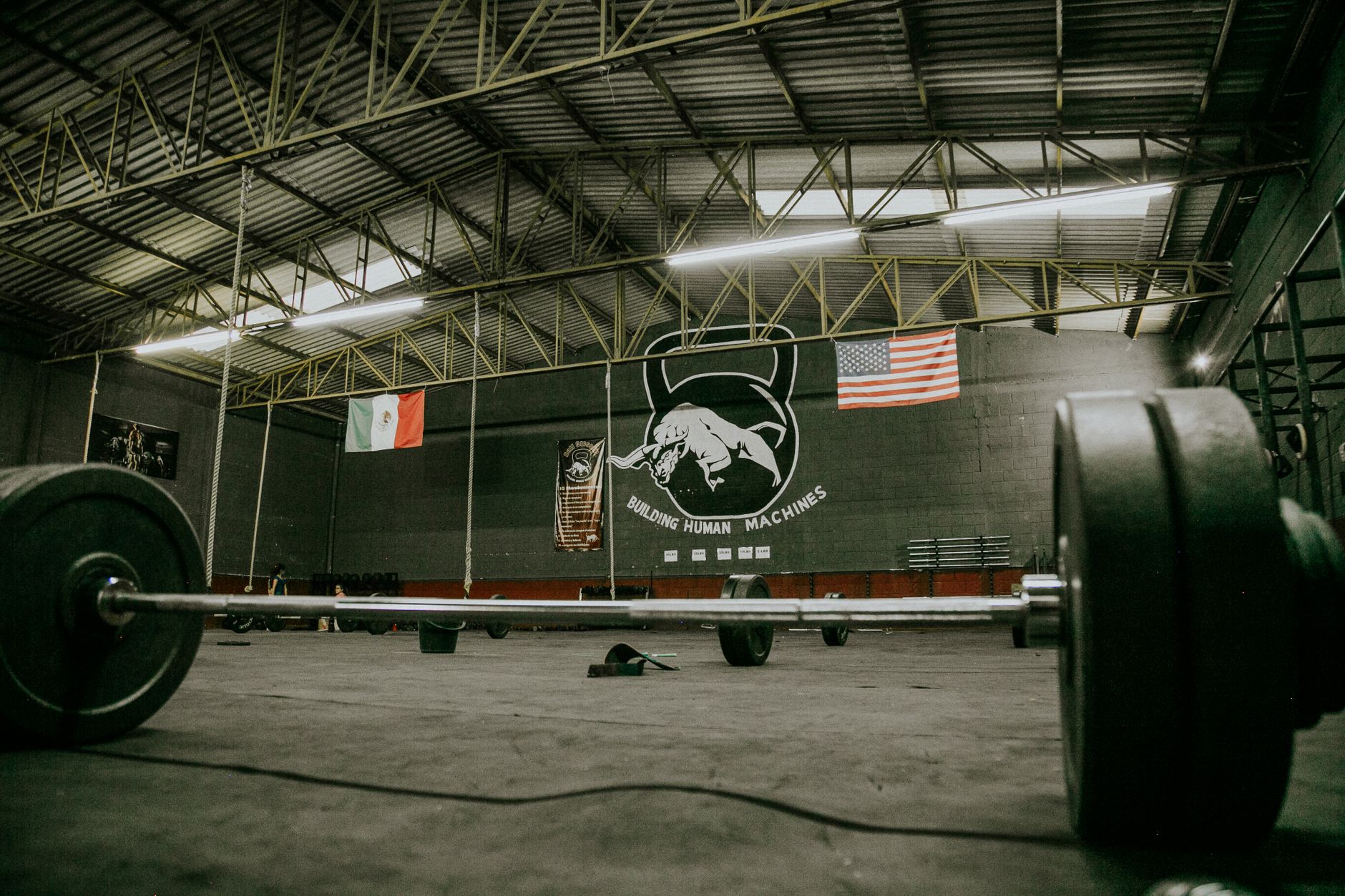 Large industrial gym interior with barbells, Mexican and American flags, and gym equipment.