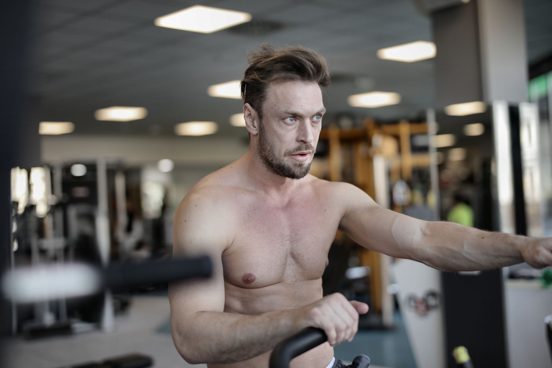 Determined male athlete with muscular body using exercise machine in modern sports center while doing cardio workout and looking away