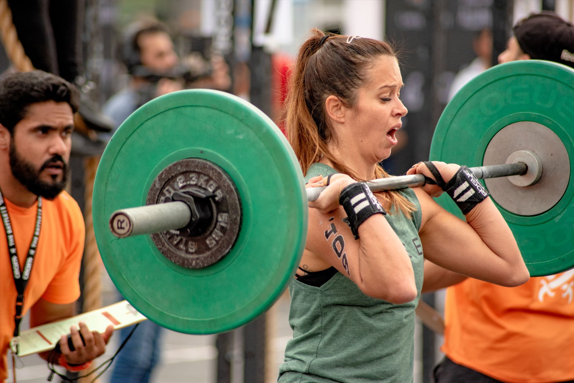 Female athlete performing weightlifting in an outdoor fitness event with spectators.