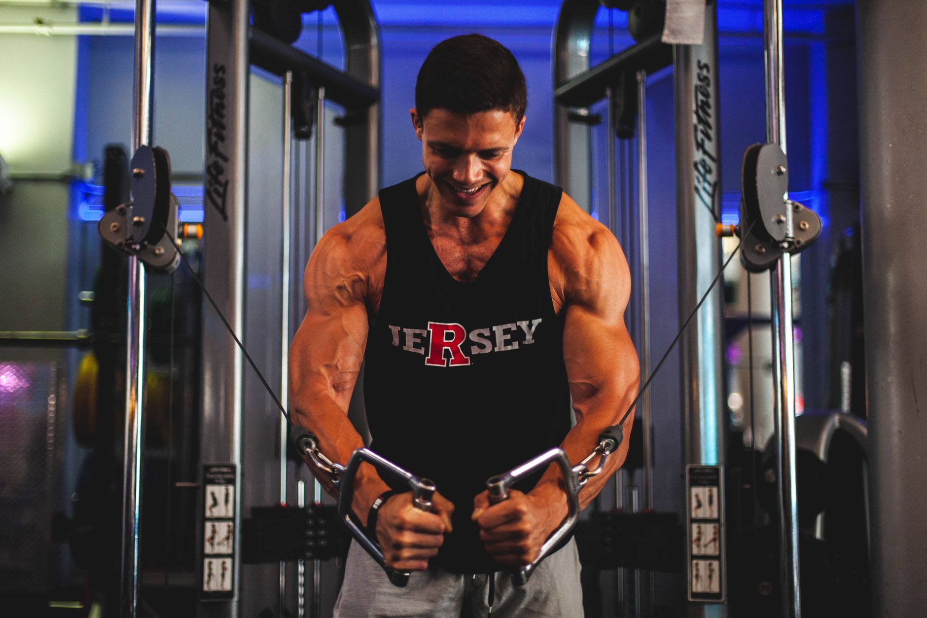 A muscular man performing exercises on a cable crossover machine in a gym.