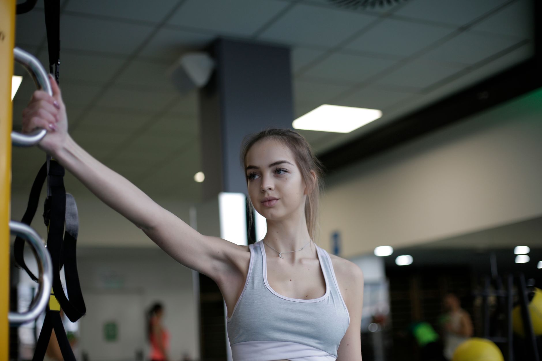 Serious young female athlete in activewear stretching arm while standing near exercise machine during workout in modern fitness center