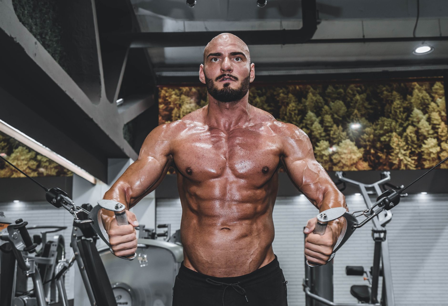 A muscular man performing cable crossover exercises in a gym setting.