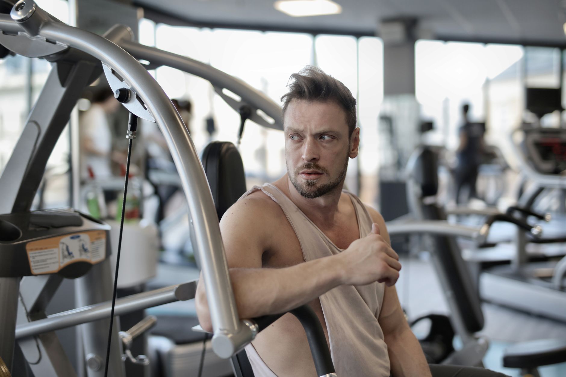 Handsome male athlete in sportswear sitting in modern fitness center and resting after training while looking away
