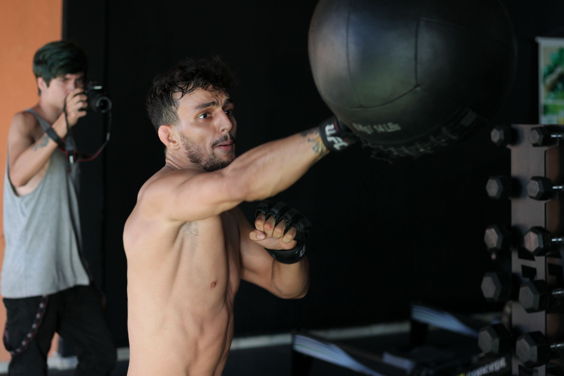 A boxer throws a punch at a heavy bag while training indoors with a camera crew.