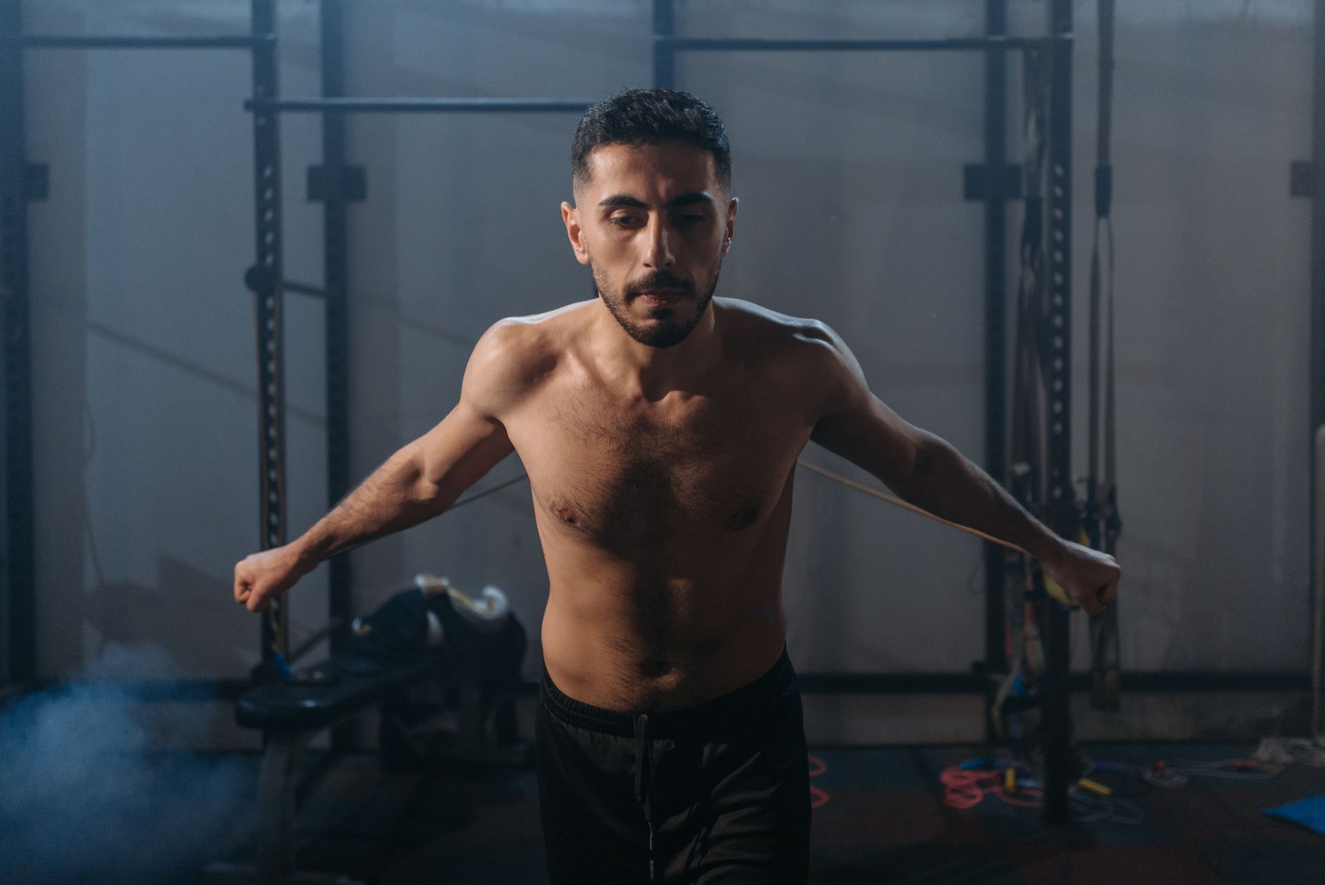 A fit young man exercises with ropes in a dimly lit gym, showcasing strength and focus.