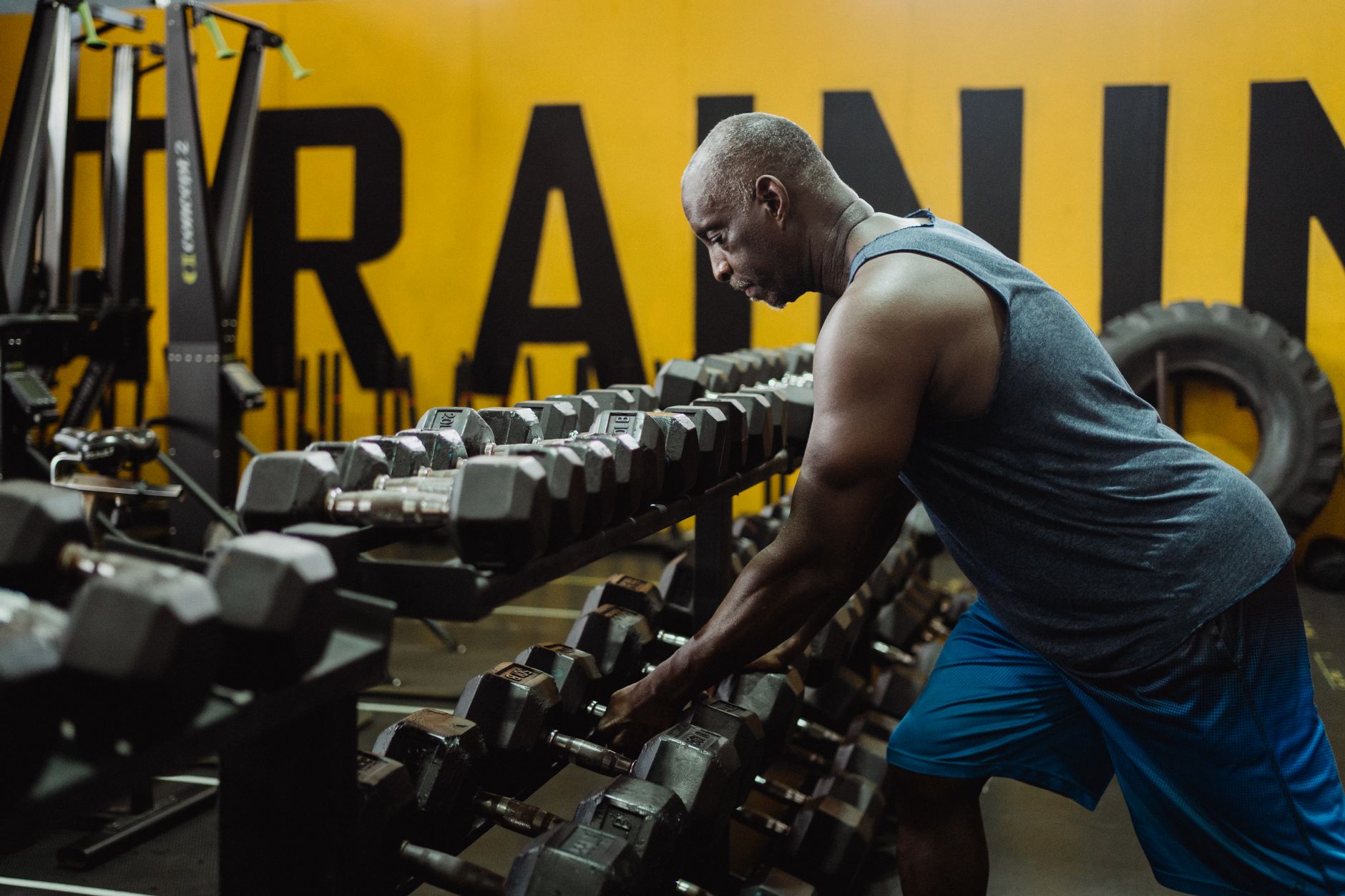 Adult man picking dumbbells from rack in a gym, focused on training and bodybuilding.