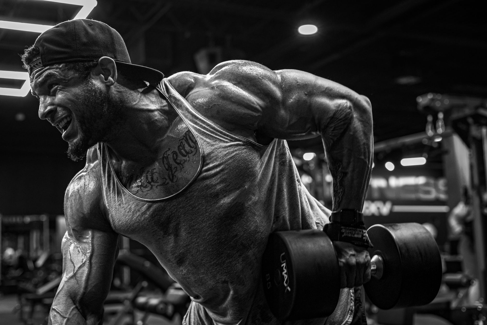 A muscular man lifting dumbbells intensely in a gym setting, showcasing strength and focus.