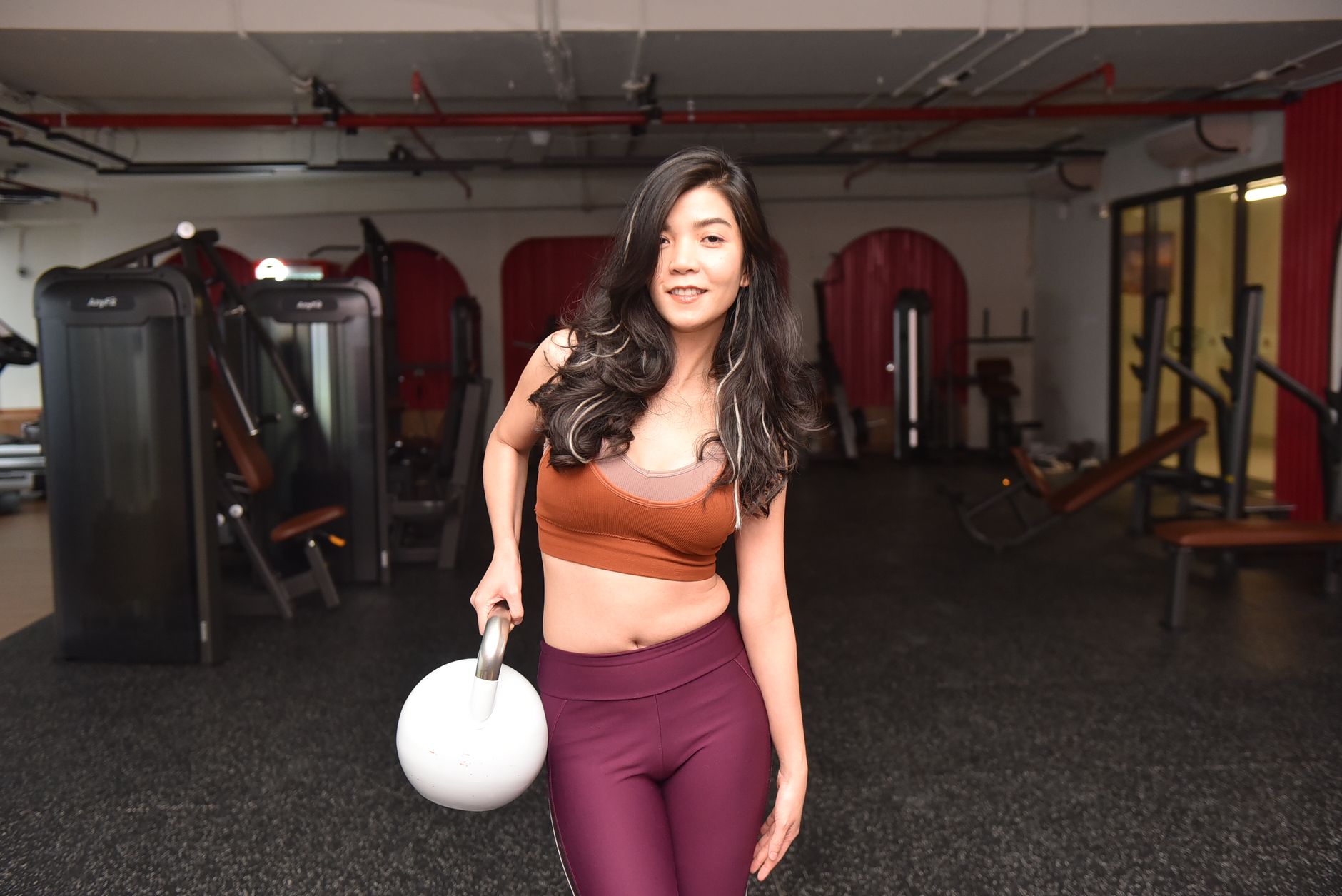 Young woman confidently lifting a kettlebell in a gym environment, promoting fitness and strength.