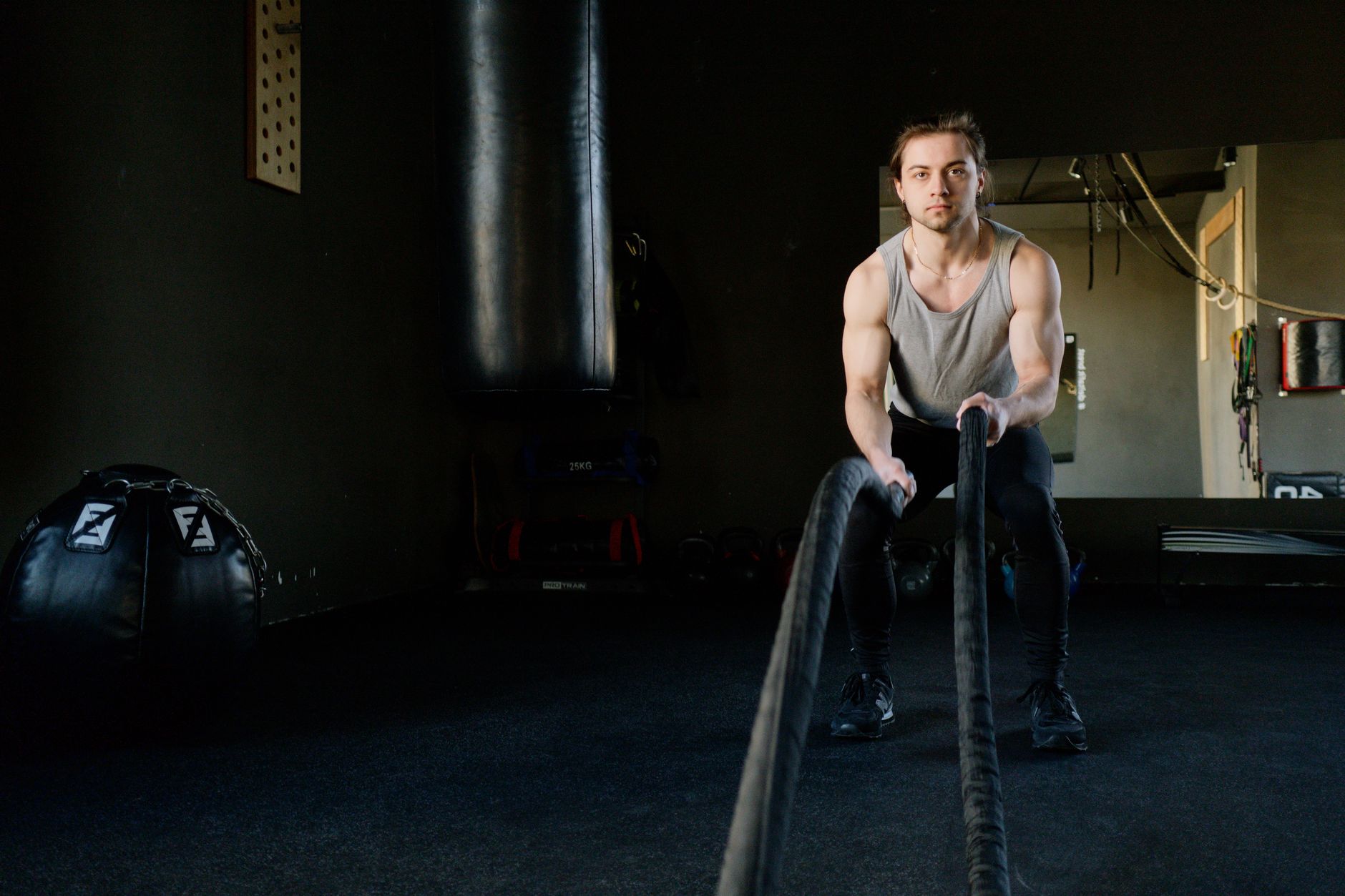 Focused young man engages in a rope workout inside a gym, enhancing strength and fitness.