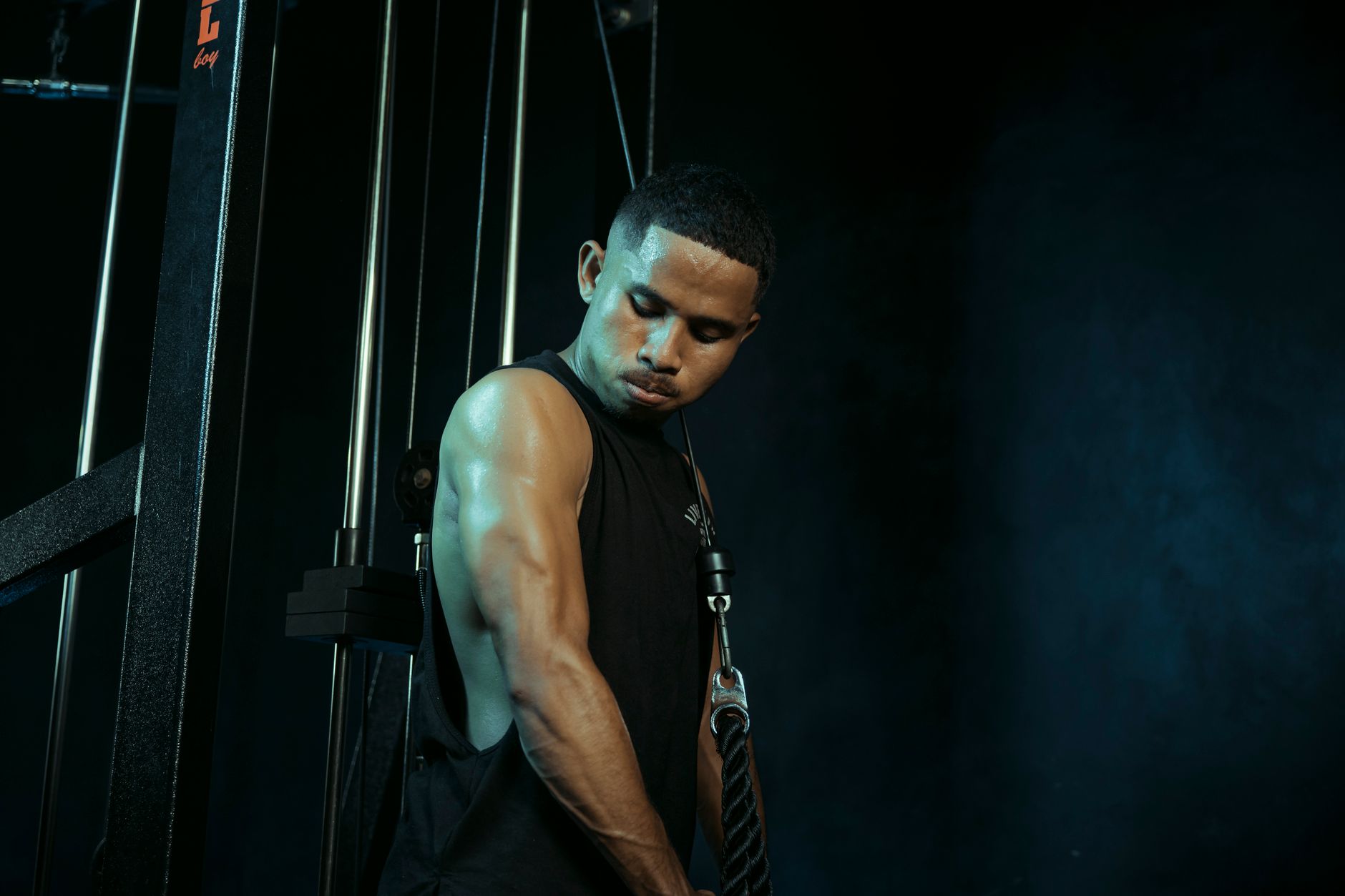 A man intensely exercising on a cable machine in a dark gym setting, highlighting fitness commitment.