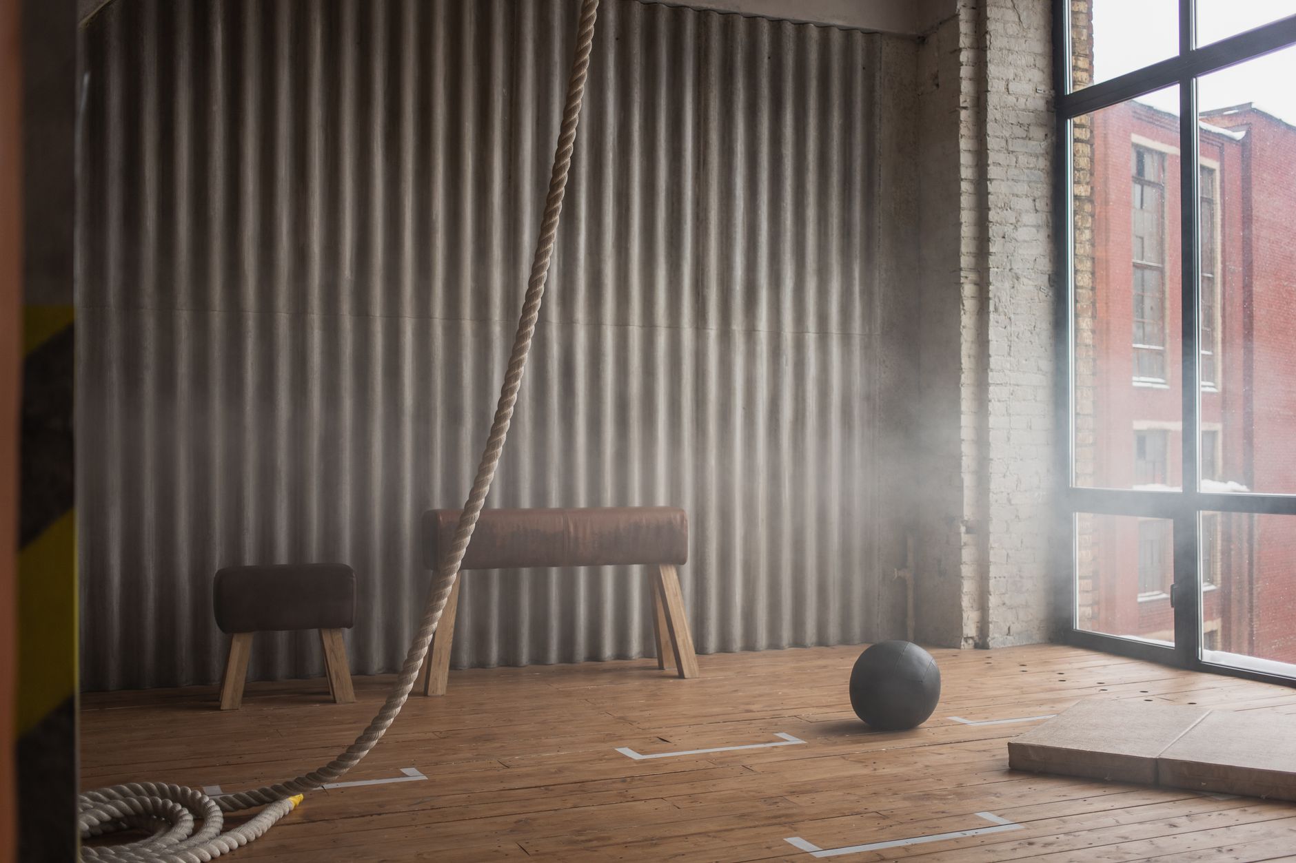 Heavy rope against weight ball and pommel horses on parquet against window in gymnasium with dust