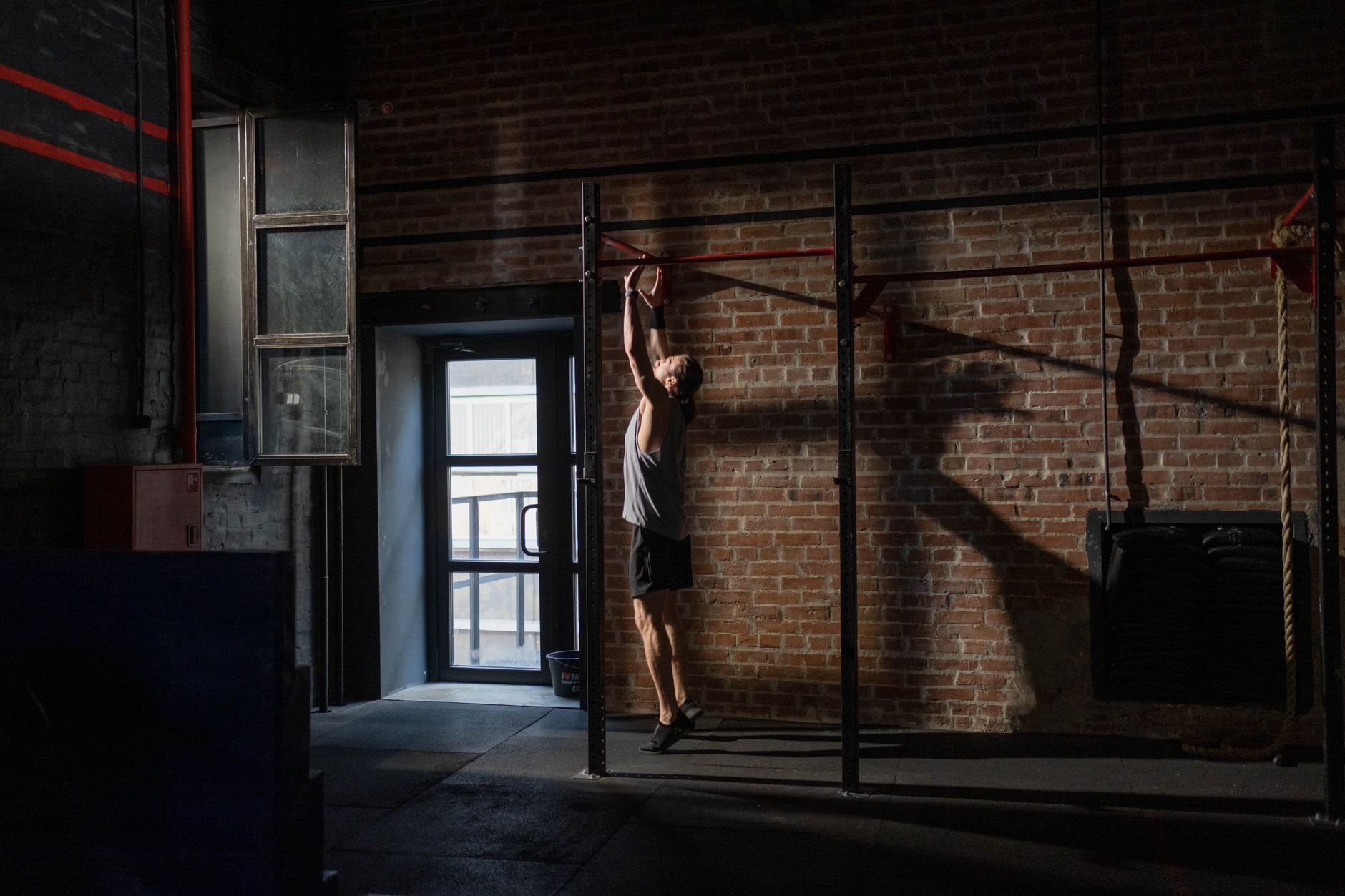 A man exercises on a pull-up bar in an industrial-style gym with brick walls, conveying fitness and dedication.