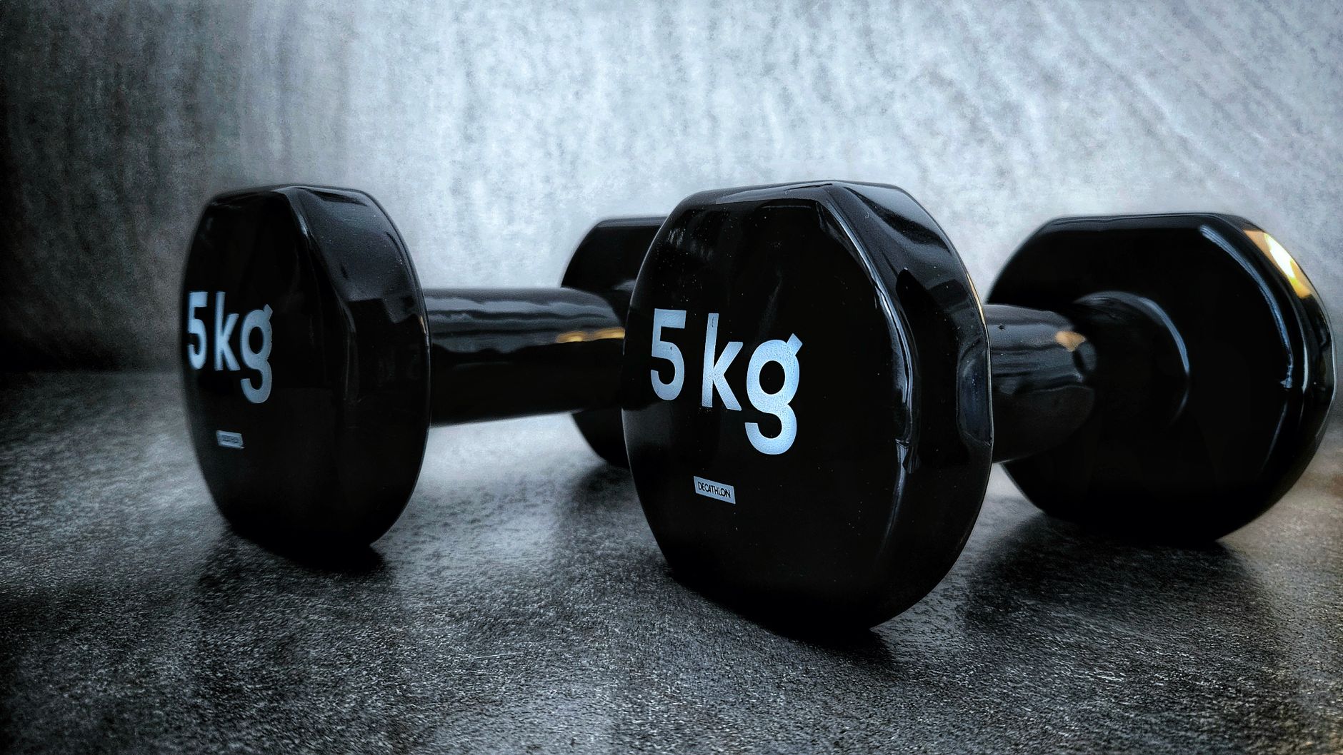 Close-up of black 5kg dumbbells on a textured dark surface, highlighting fitness and strength training equipment.