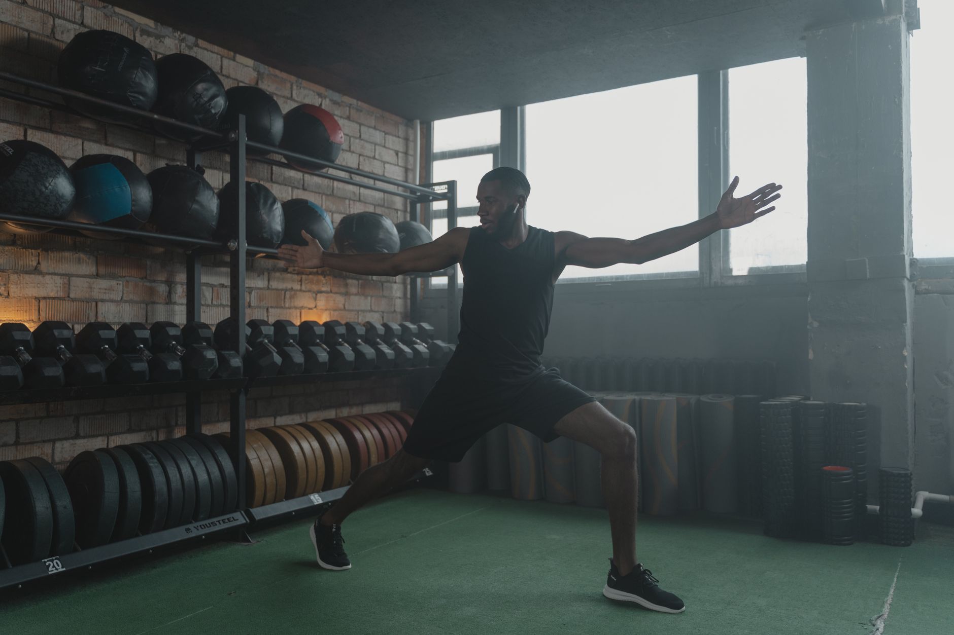 A muscular black man stretching in a modern gym with fitness equipment, promoting healthy living.