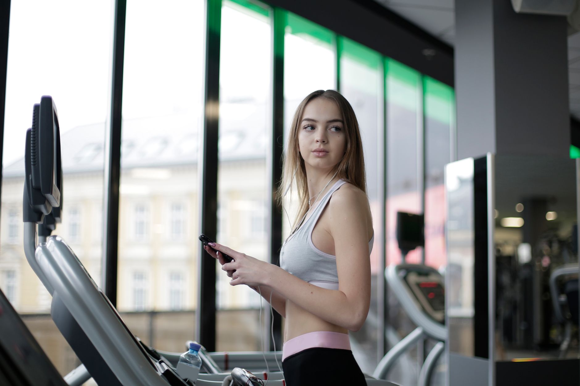 Young woman working out on a treadmill in a gym with large windows. Fitness-focused lifestyle.