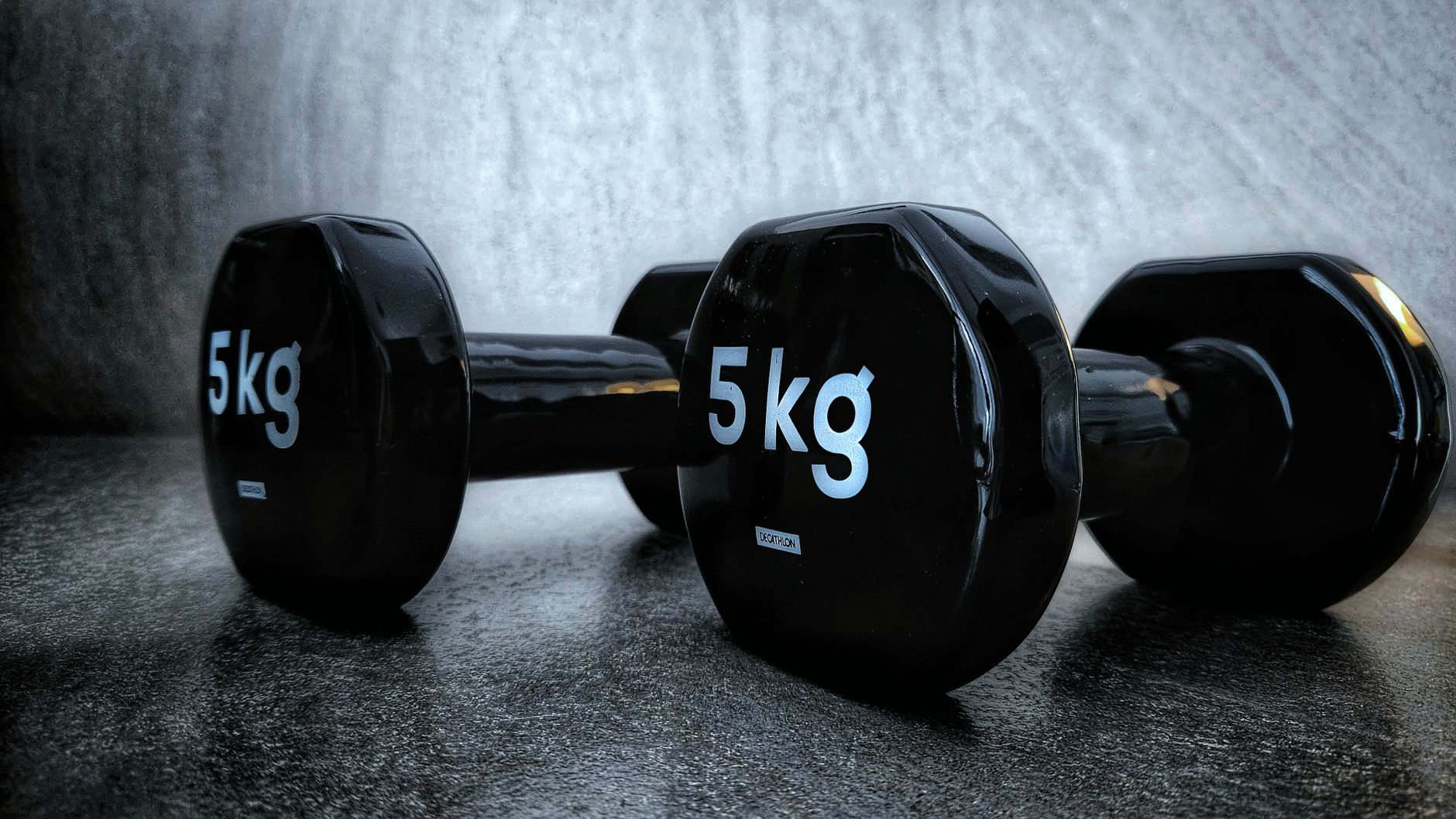 Close-up of two 5kg dumbbells on a textured dark background, showcasing fitness equipment.