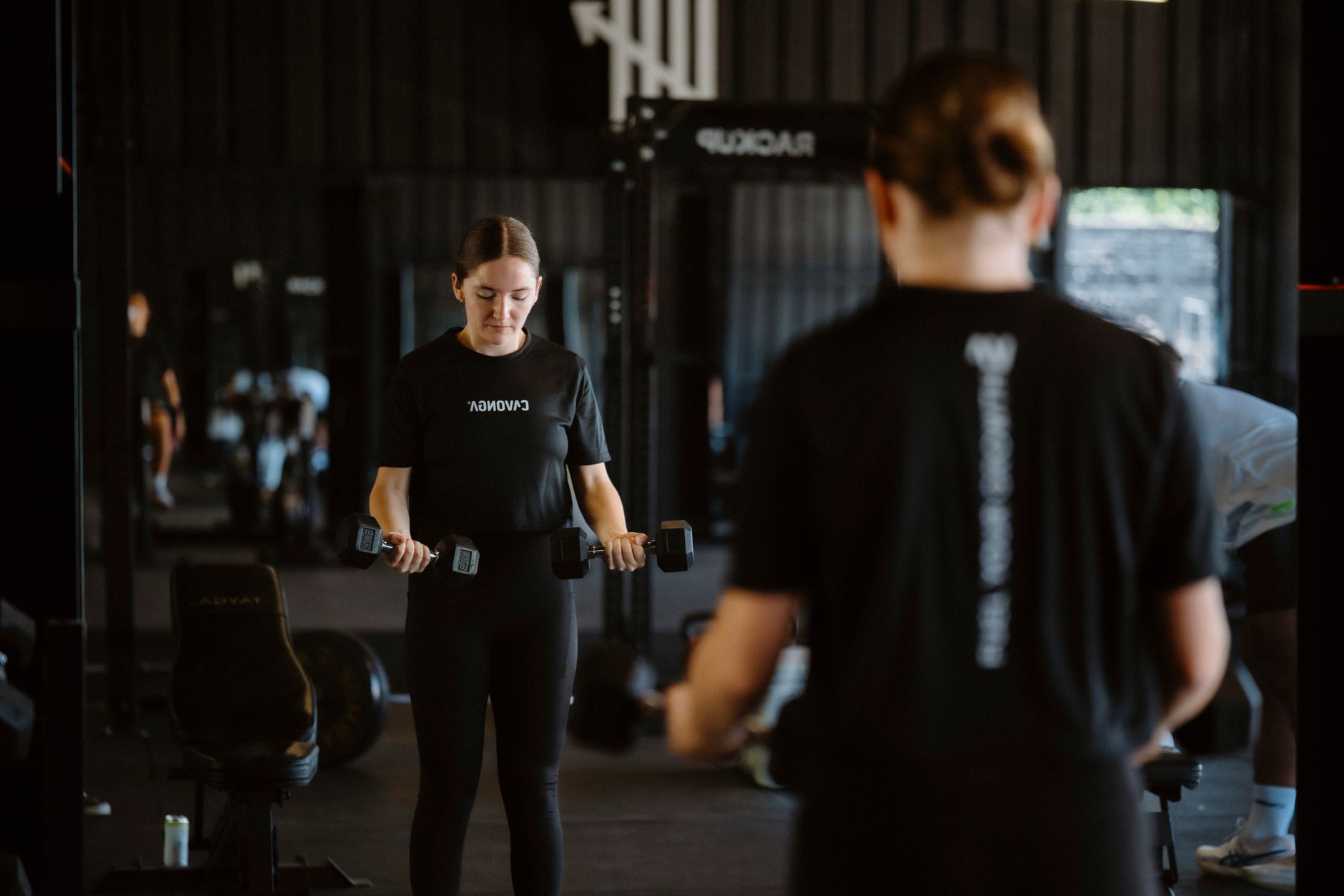 A woman performing a focused dumbbell workout in a modern gym setting.