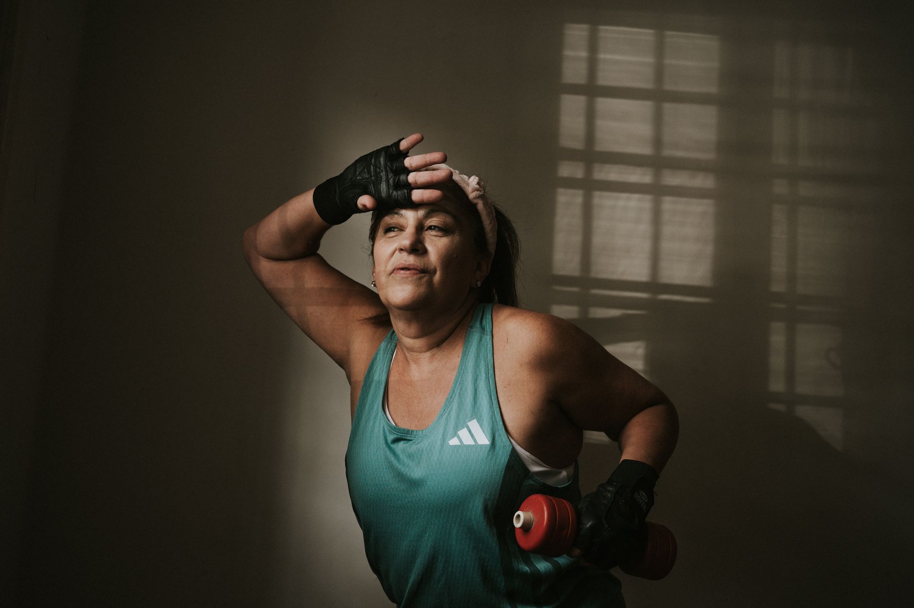 Middle-aged woman in workout attire holding dumbbells, exercising indoors with focused expression.