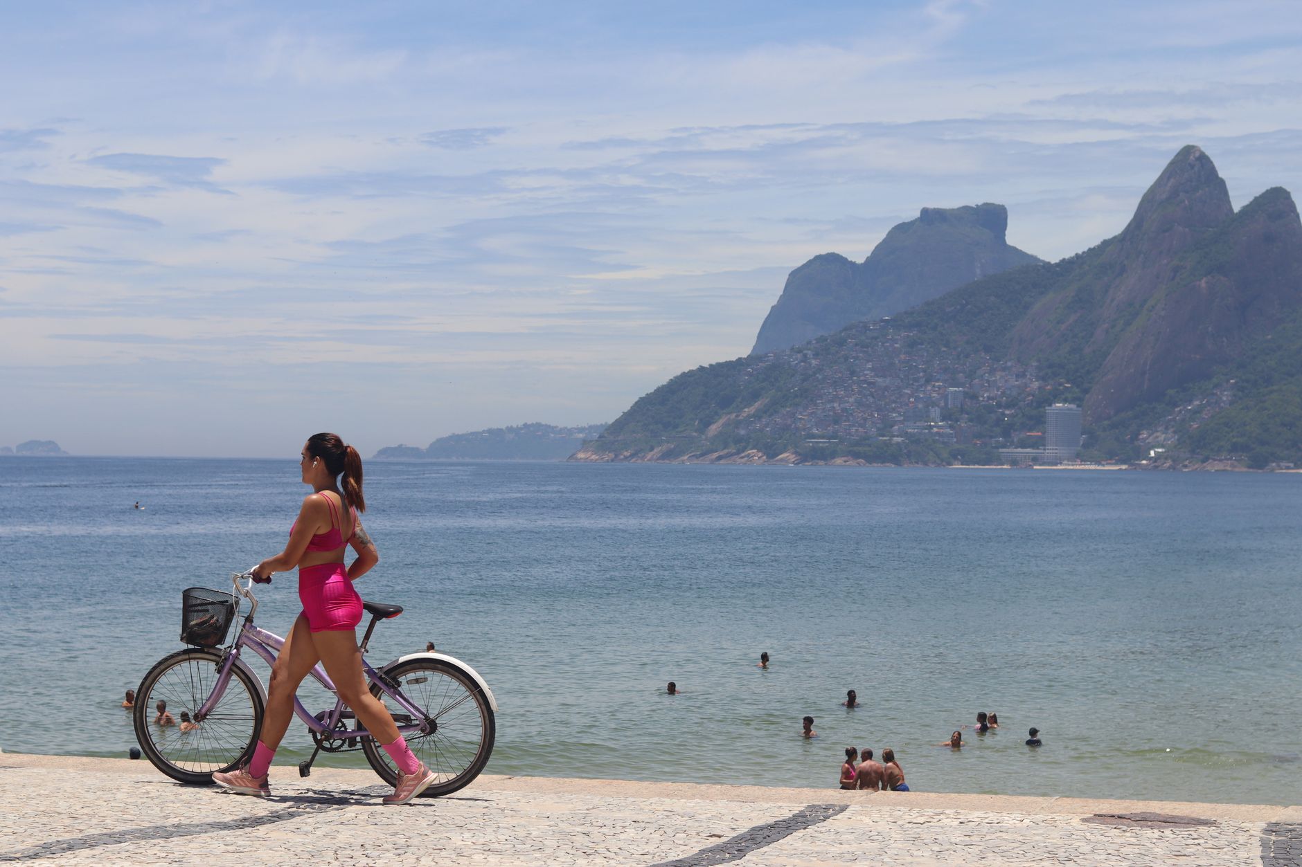Woman on a bicycle enjoying a sunny day by the seaside with mountains in the distance.