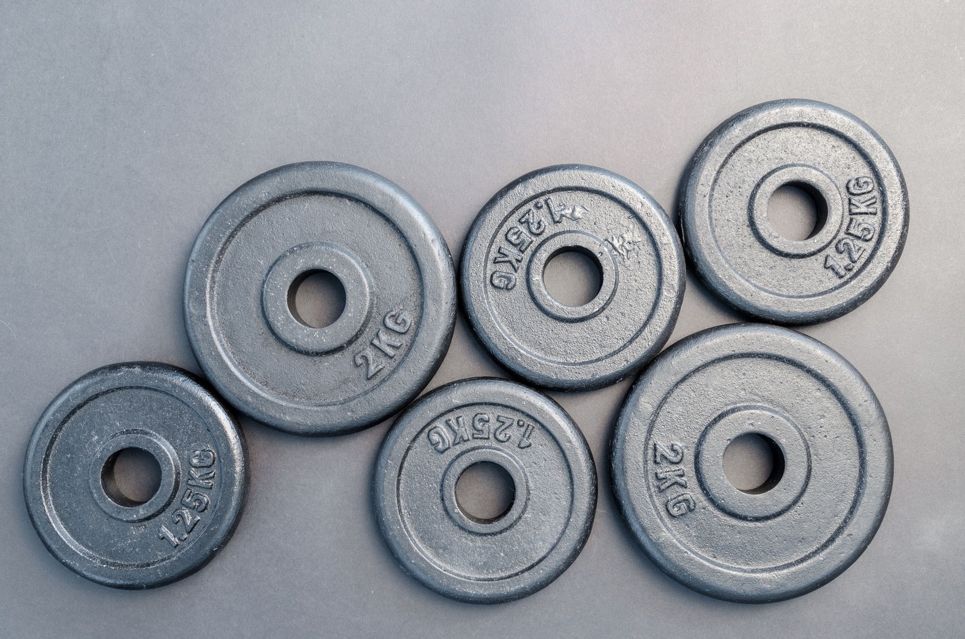 Close-up of steel gym weight plates in various sizes arranged on a gray surface.