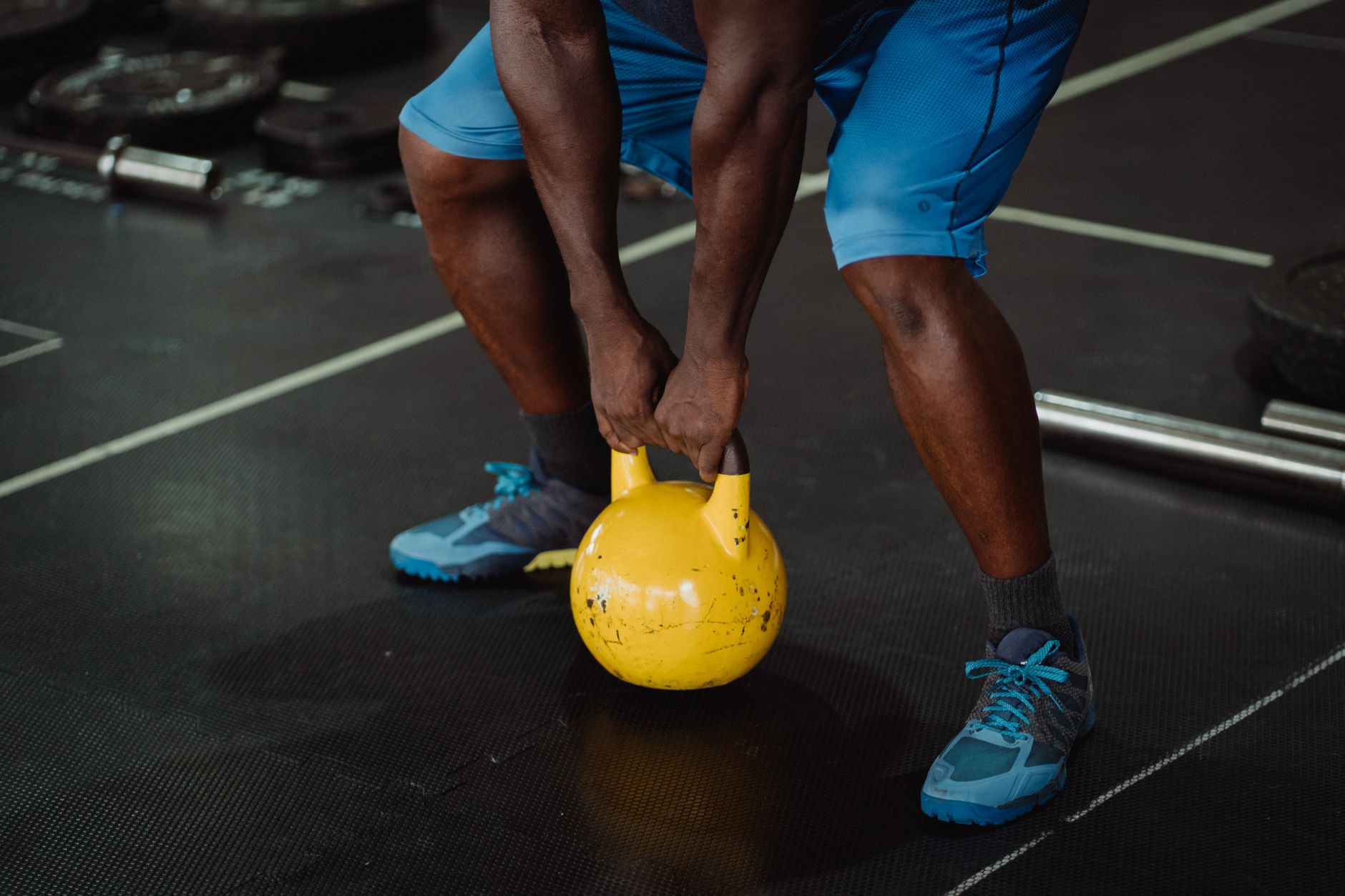 Person lifting a yellow kettlebell in a gym setting, promoting fitness and strength.