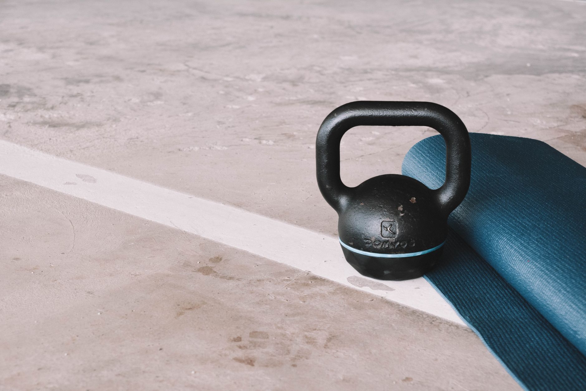 Kettlebell and blue yoga mat on a concrete floor in an indoor gym setting.