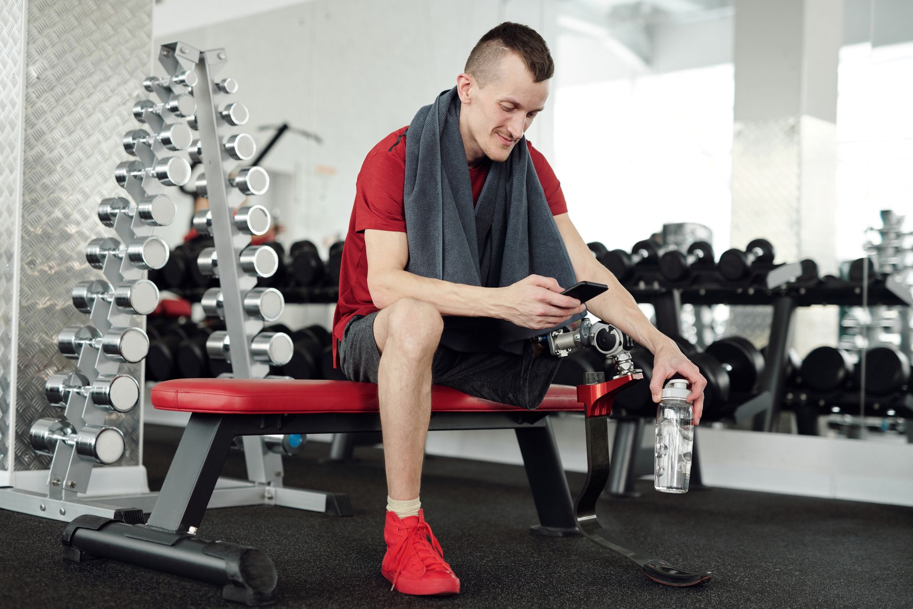 Active man with prosthetic leg taking a break in the gym, checking phone.