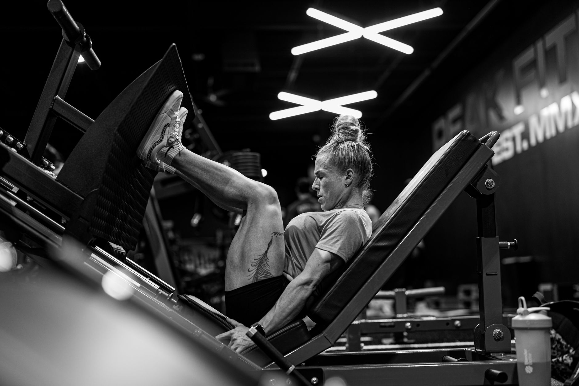 Black and white photo of a woman intensely focusing while doing a leg press exercise in a gym.