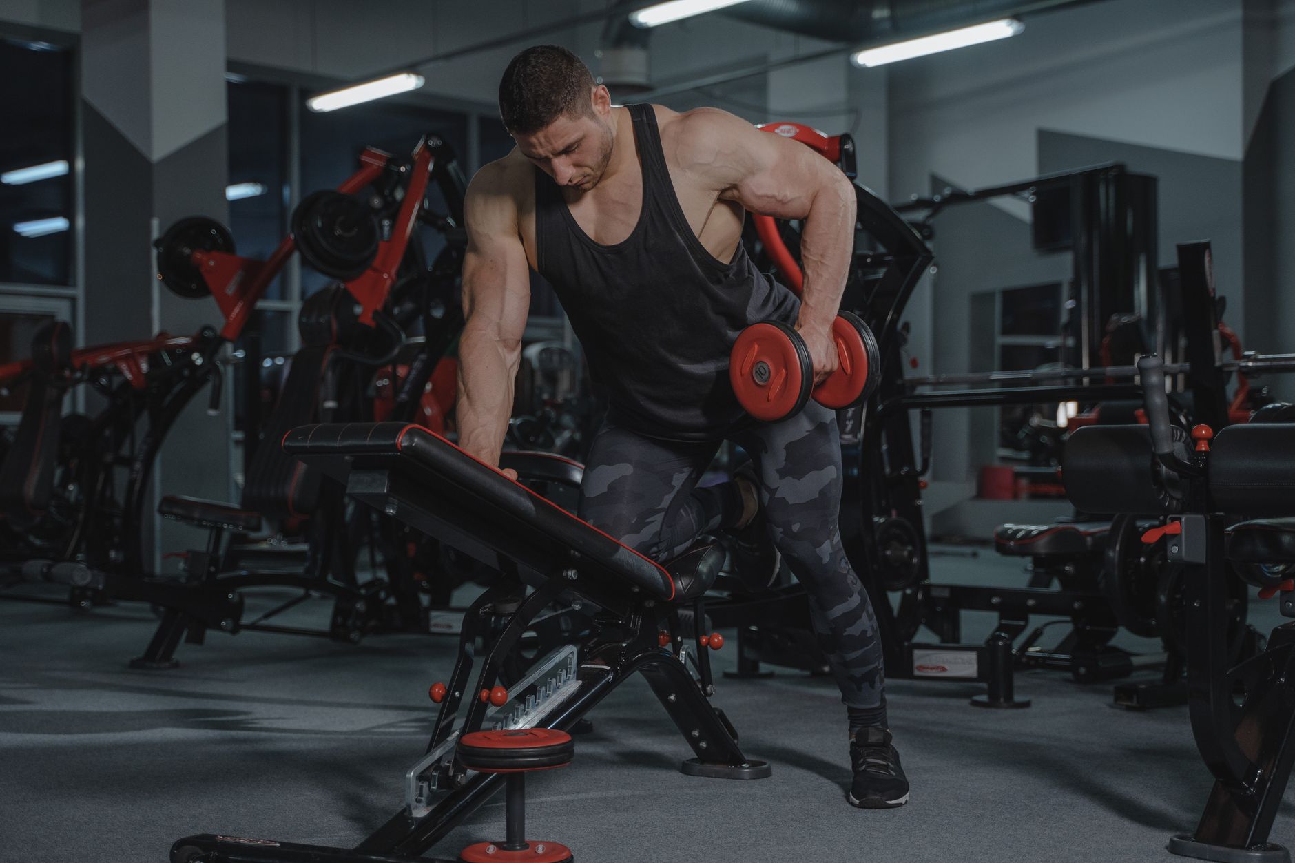 A strong, muscular man lifting dumbbells in a modern gym environment.